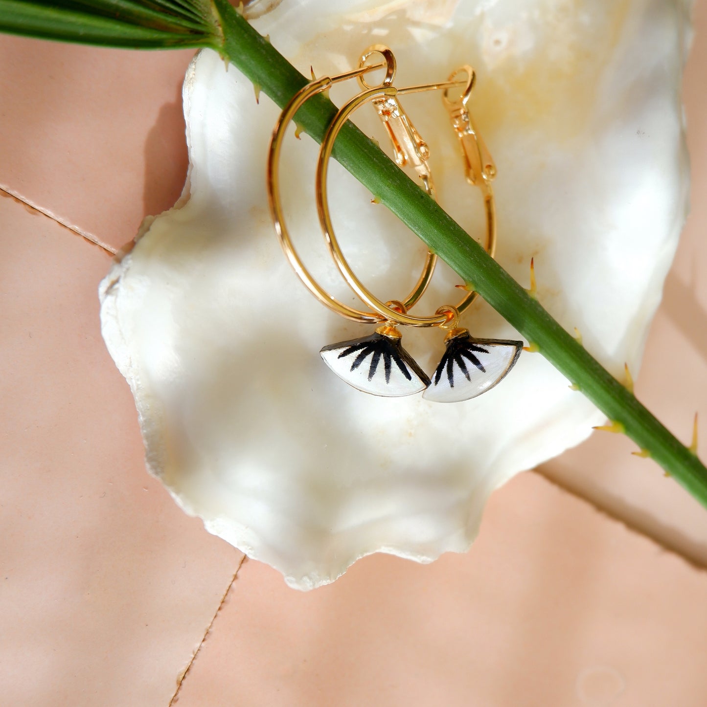 small gold hoop earrings with black spiky palm design on mother of pearl, in oyster shell