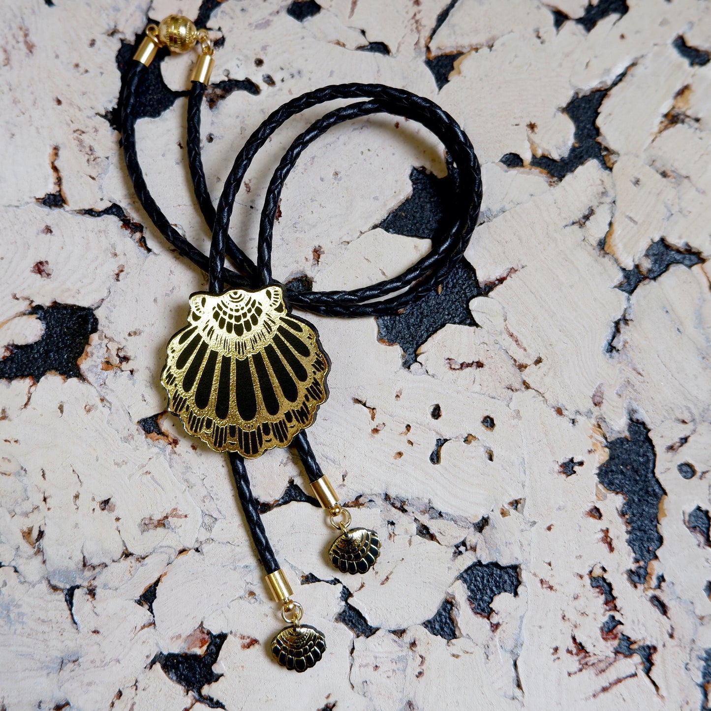 leather shell bolo necklace in black, on white & black cork background