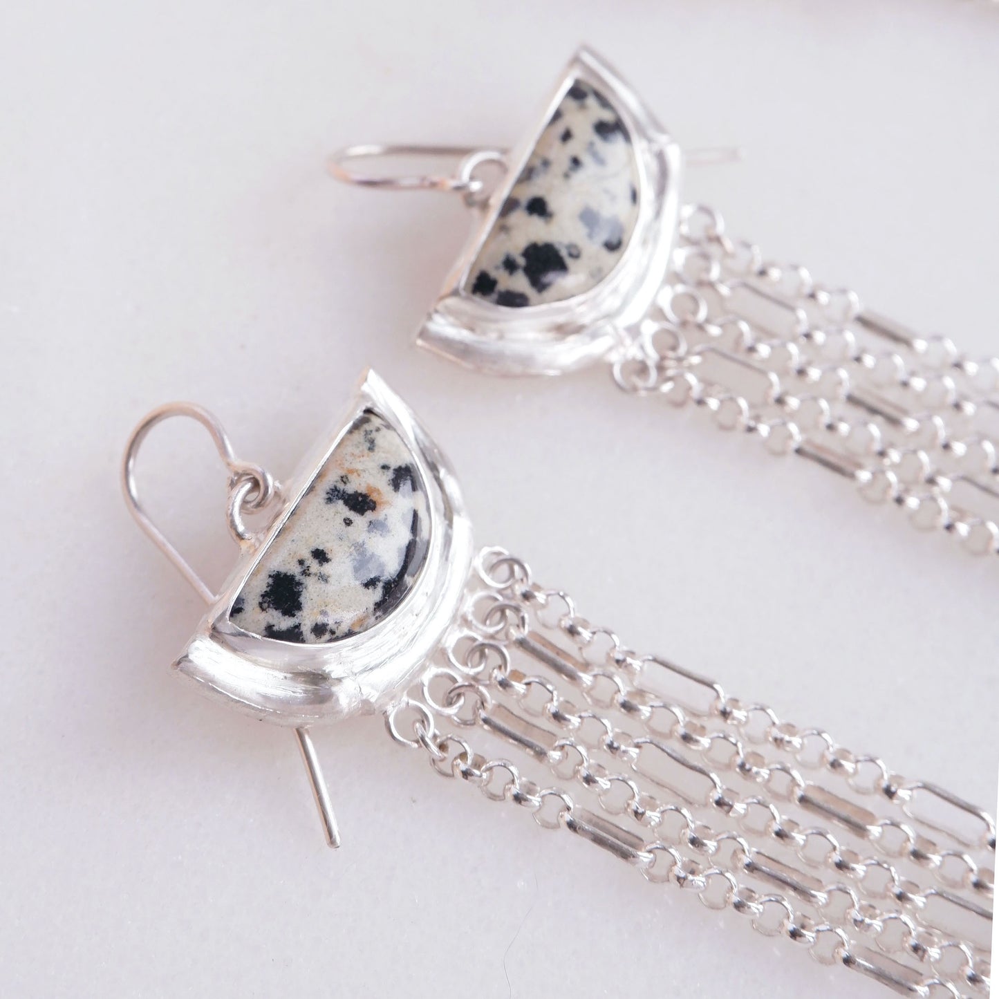 dramatic long chain fringe chandelier tassel earrings with half moon shaped semi precious speckled dalmatian jasper gemstones, cupped by solid silver bamboo hammock, with simple silver wire hooks. close up cropped shot