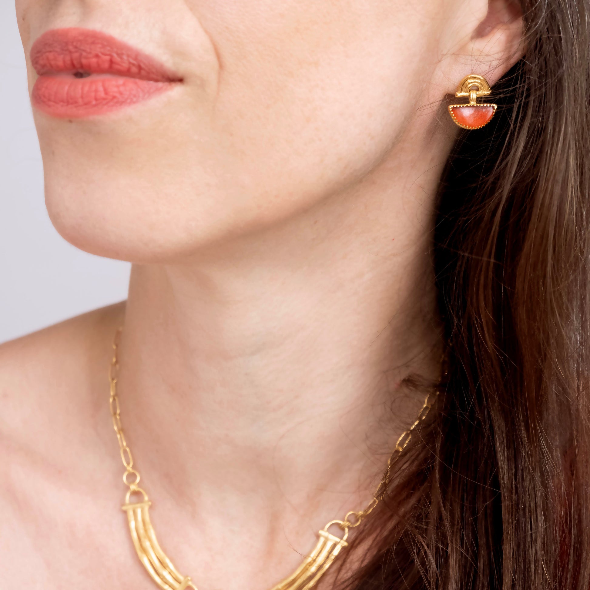 small stud earrings in gold vermeil, featuring triple arches of bamboo, hung with a half moon shaped Carnelian gemstone, set with gold teeth, on model