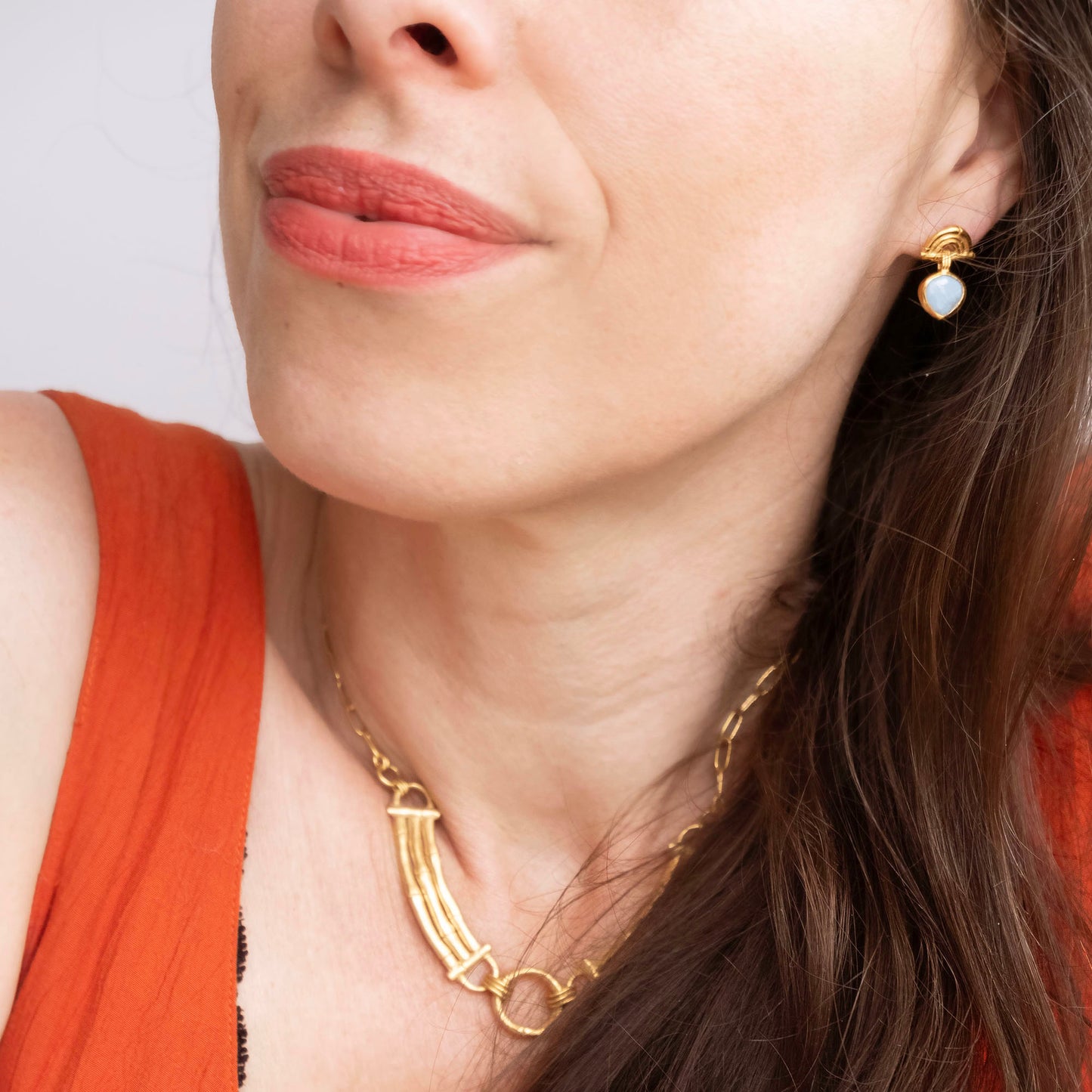 small stud earrings in gold vermeil, featuring triple arches of bamboo, hung with a faceted blue opal gemstone pendant, on model