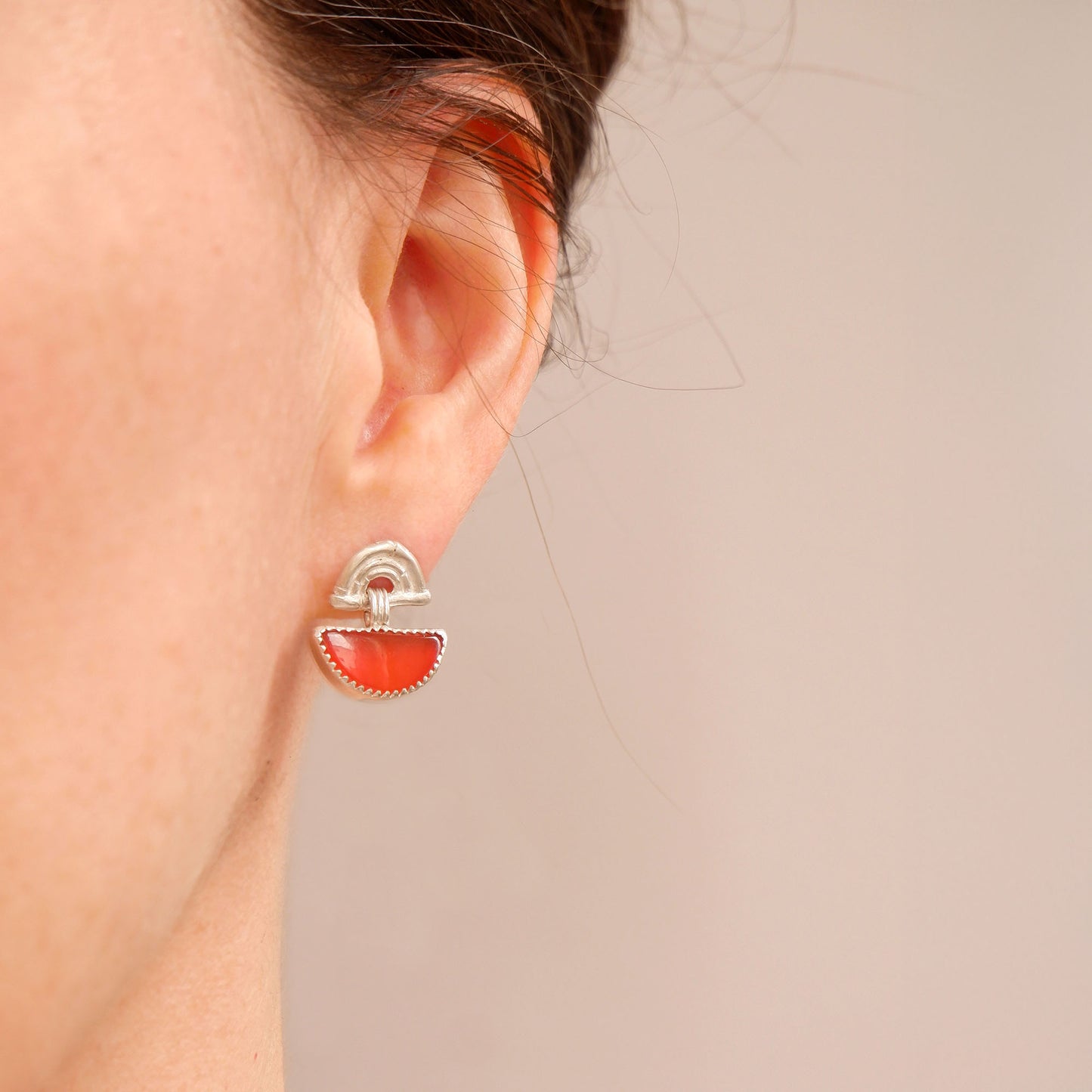 small stud earrings in sterling silverl, featuring triple arches of bamboo, hung with a half moon shaped Carnelian gemstone, set with silver teeth, on model