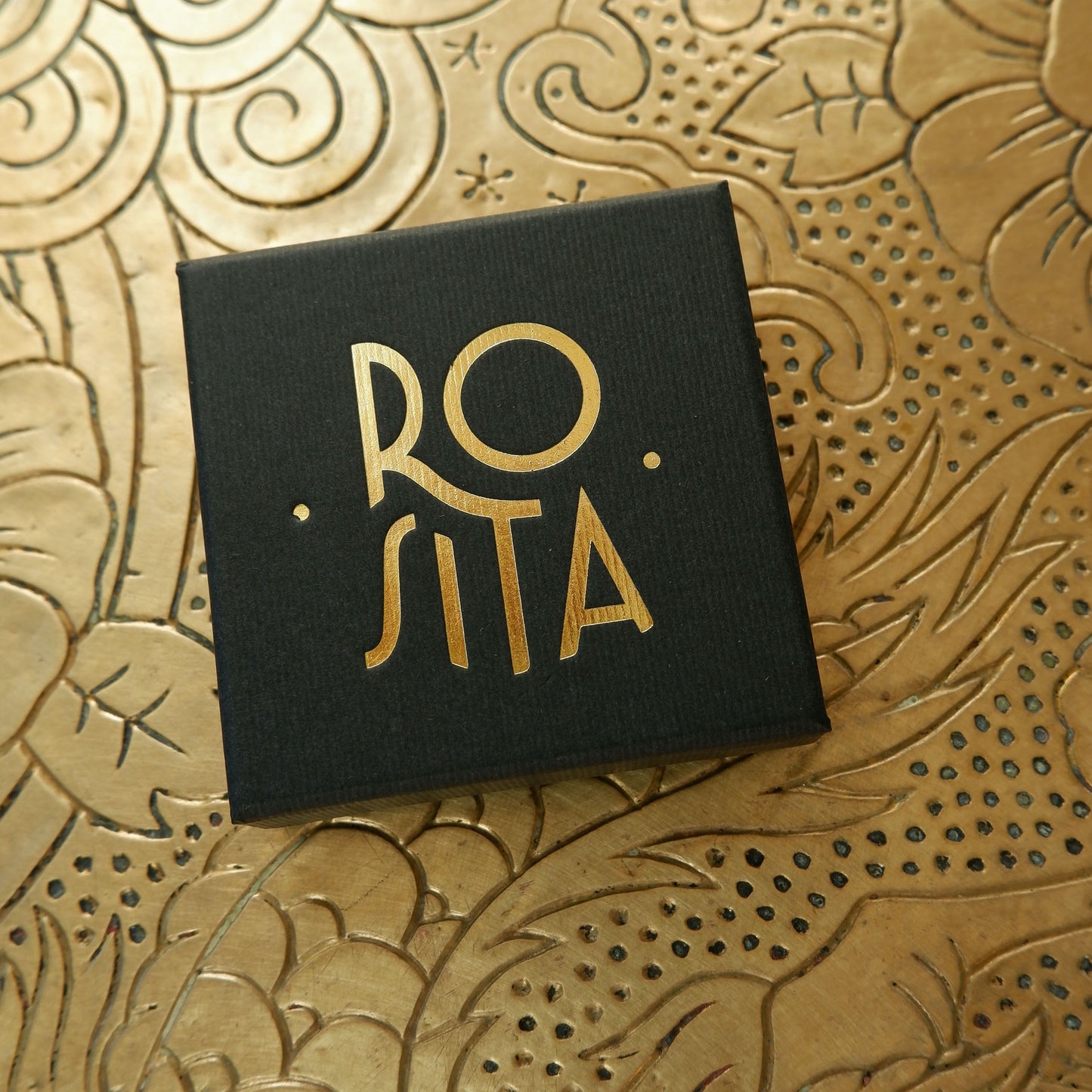Black finely ribbed cardboard jewellery box, with ROSITA logo branding in Gold foil, on gold patterned background