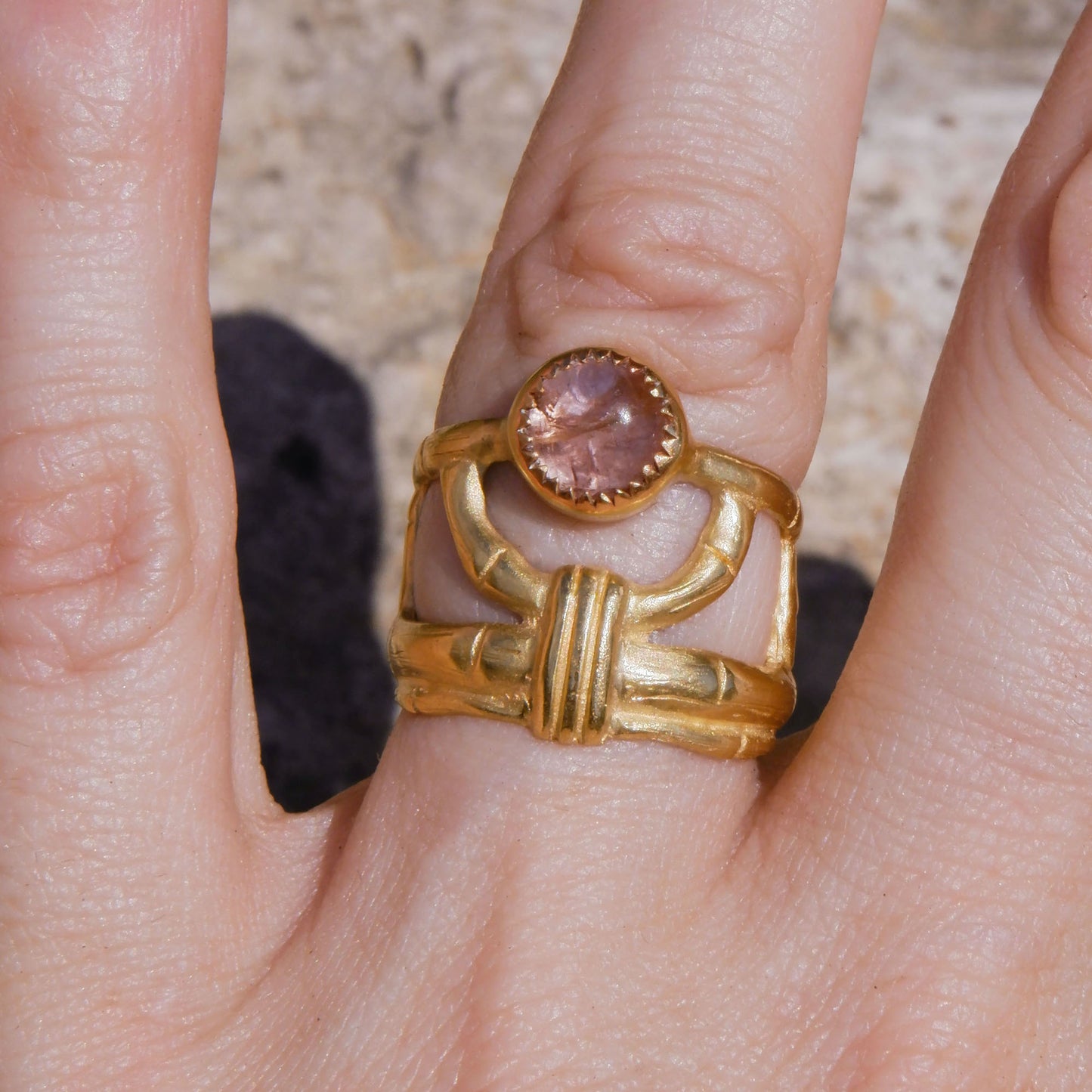 structural open-work ring in a bamboo style, featuring round pale peachy pink Tourmaline cabochon gemstone in a serrated setting. Gold Vermeil. Shown sitting on a hand for scale