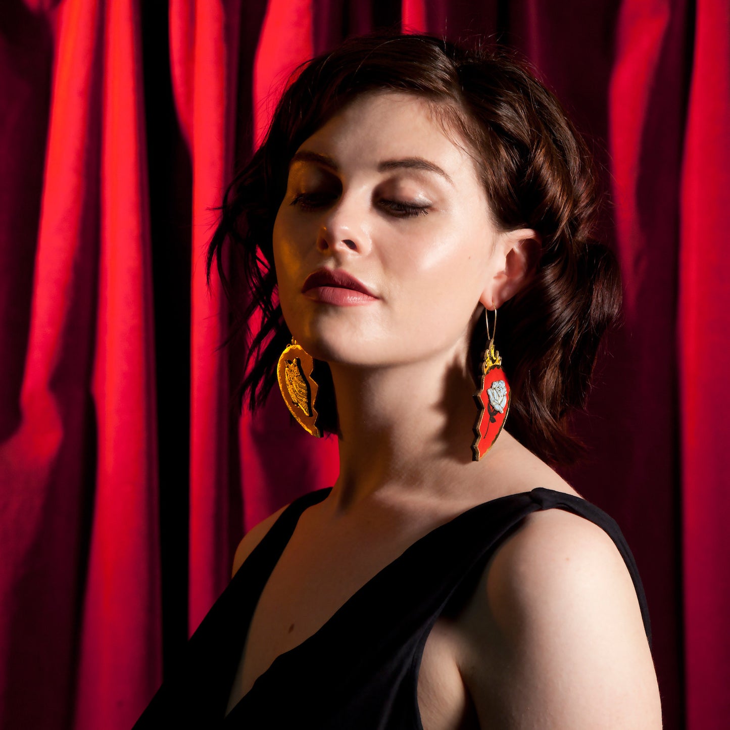 red leather broken heart pendants & earrings, with golden owls, flames & blue roses on model, against red velvet curtain