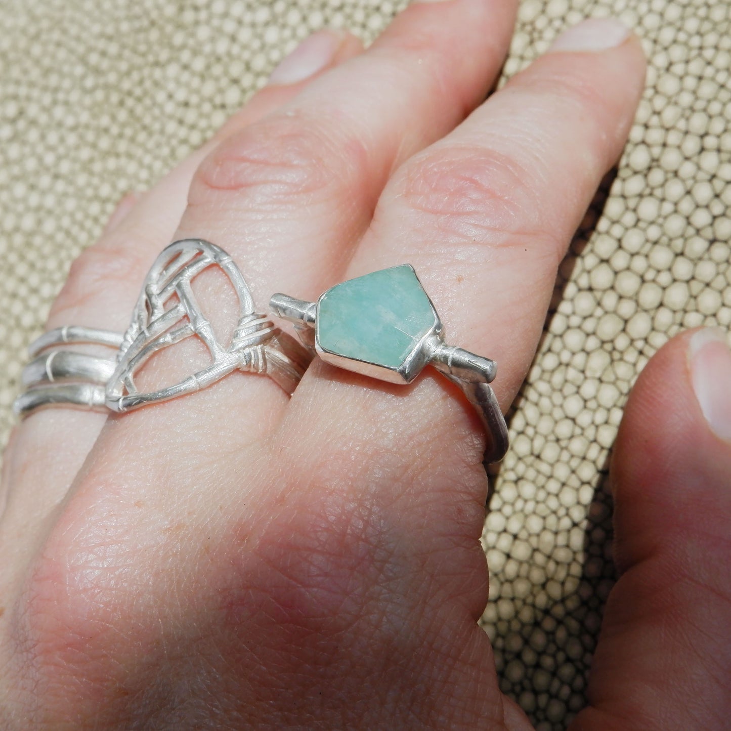 Sterling Silver flat top bamboo style ring with a an irregular angular geometric Amazonite gem stone, on a whand, with other sterling silver bamboo style rings, against a textured background