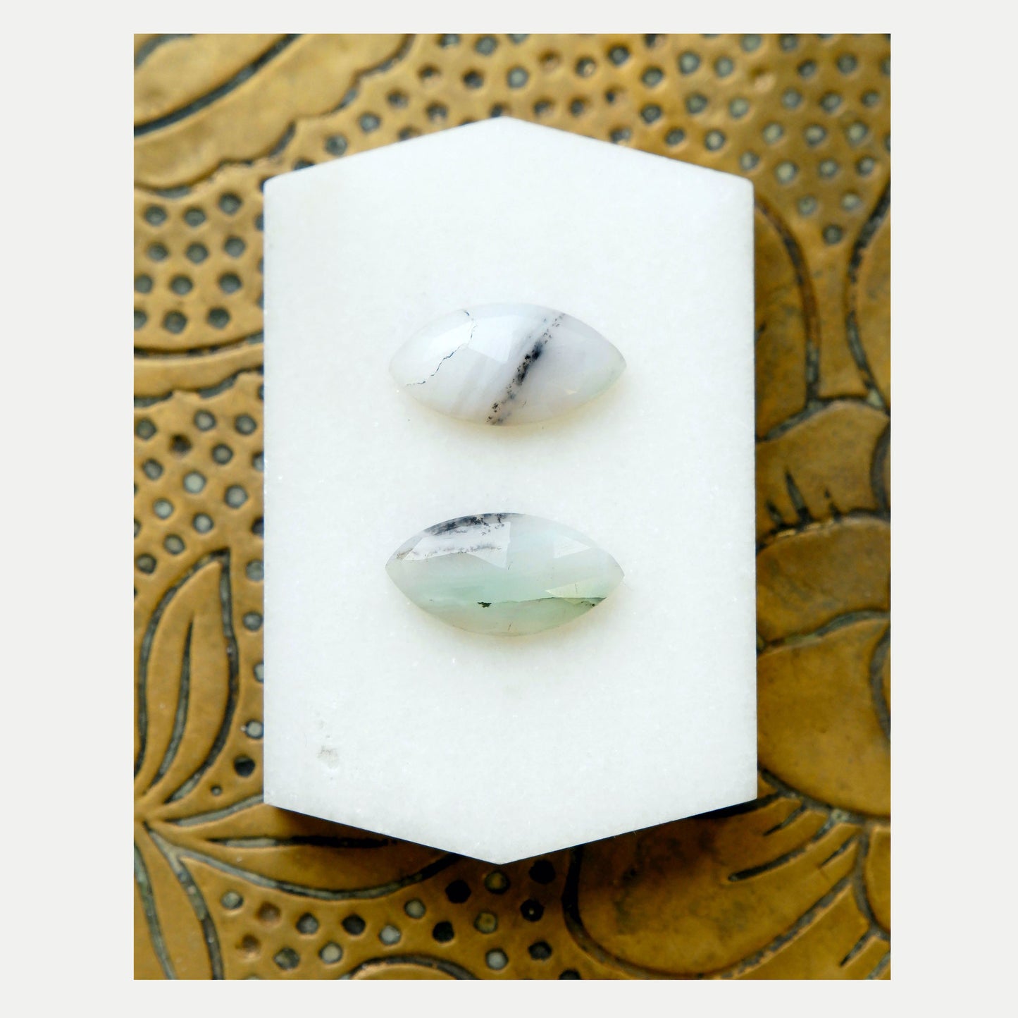 two Marquise-Cut faceted pale Green Peruvian Opal Gemstones, with delicate but distinctive black marbling. Shown on white tile.