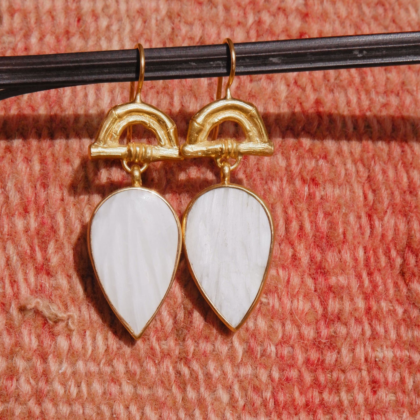 Gold Vermeil hook earrings featuring bamboo sunrise arch design, with pointed gemstone drop pendants in white scolecite, shown on woven pink background
