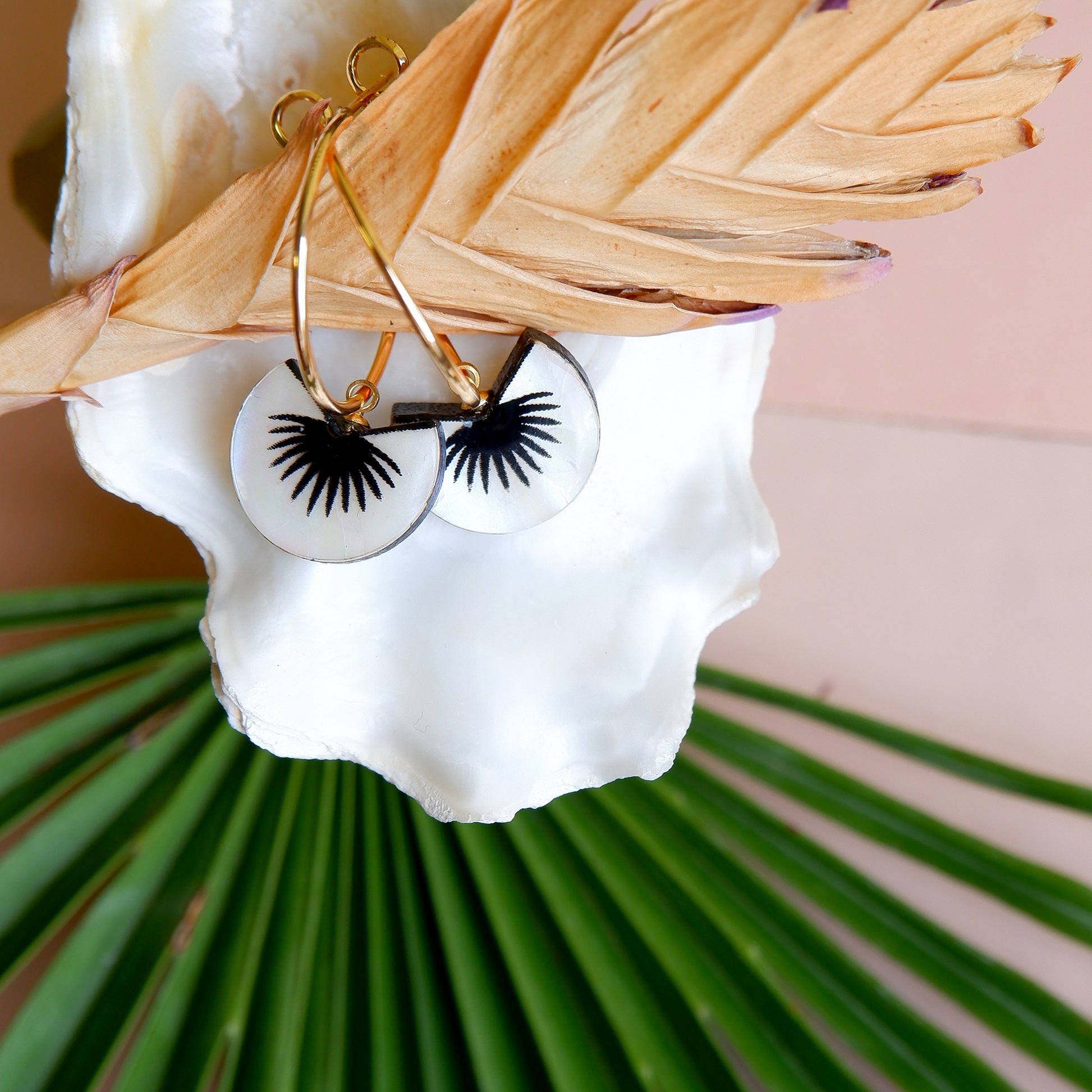 graphic black & mother of pearl spiky palm leaf design pendants on gold hoop earrings, lifestyle shot with oyster shell & palm leaf