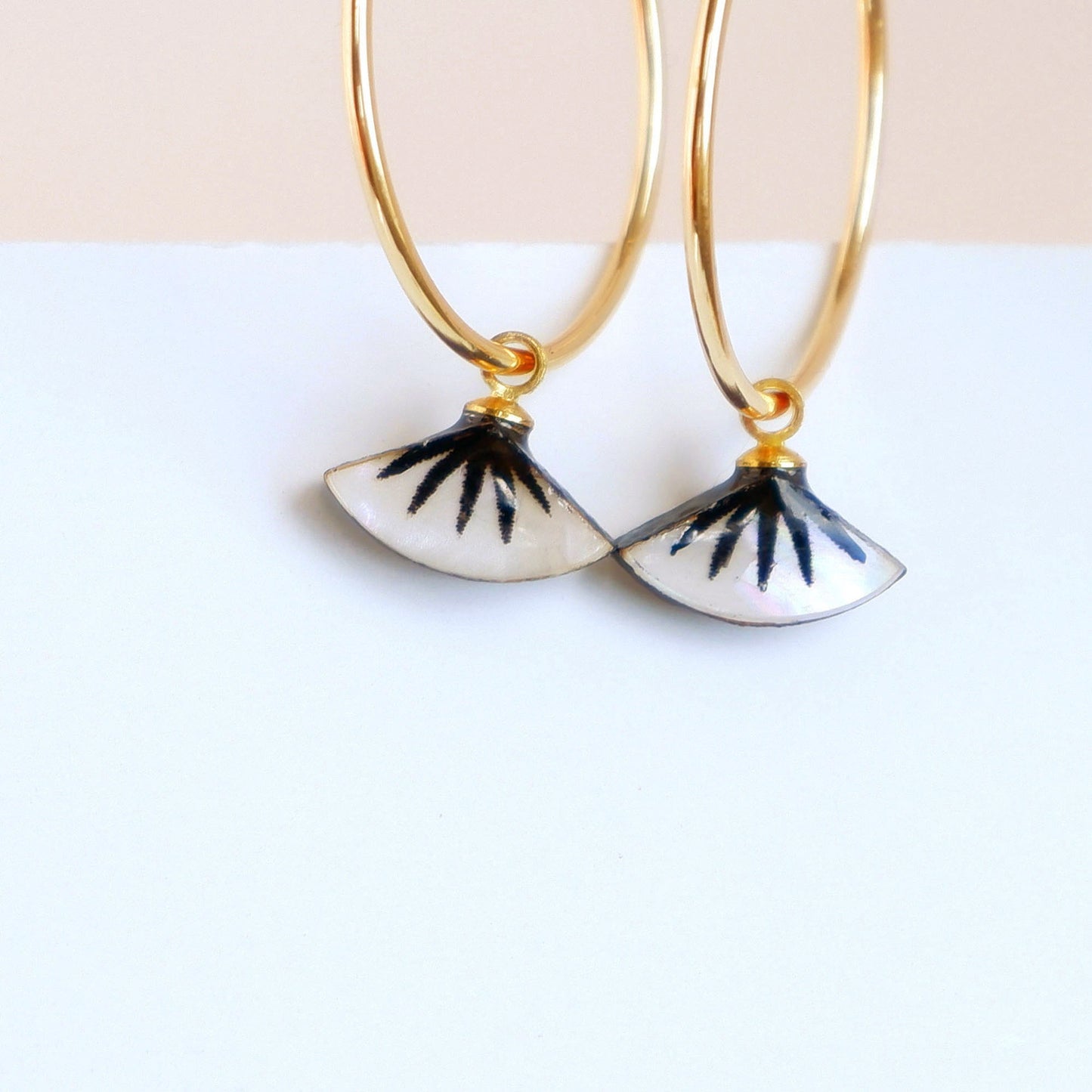 small gold hoop earrings with black spiky palm design on mother of pearl