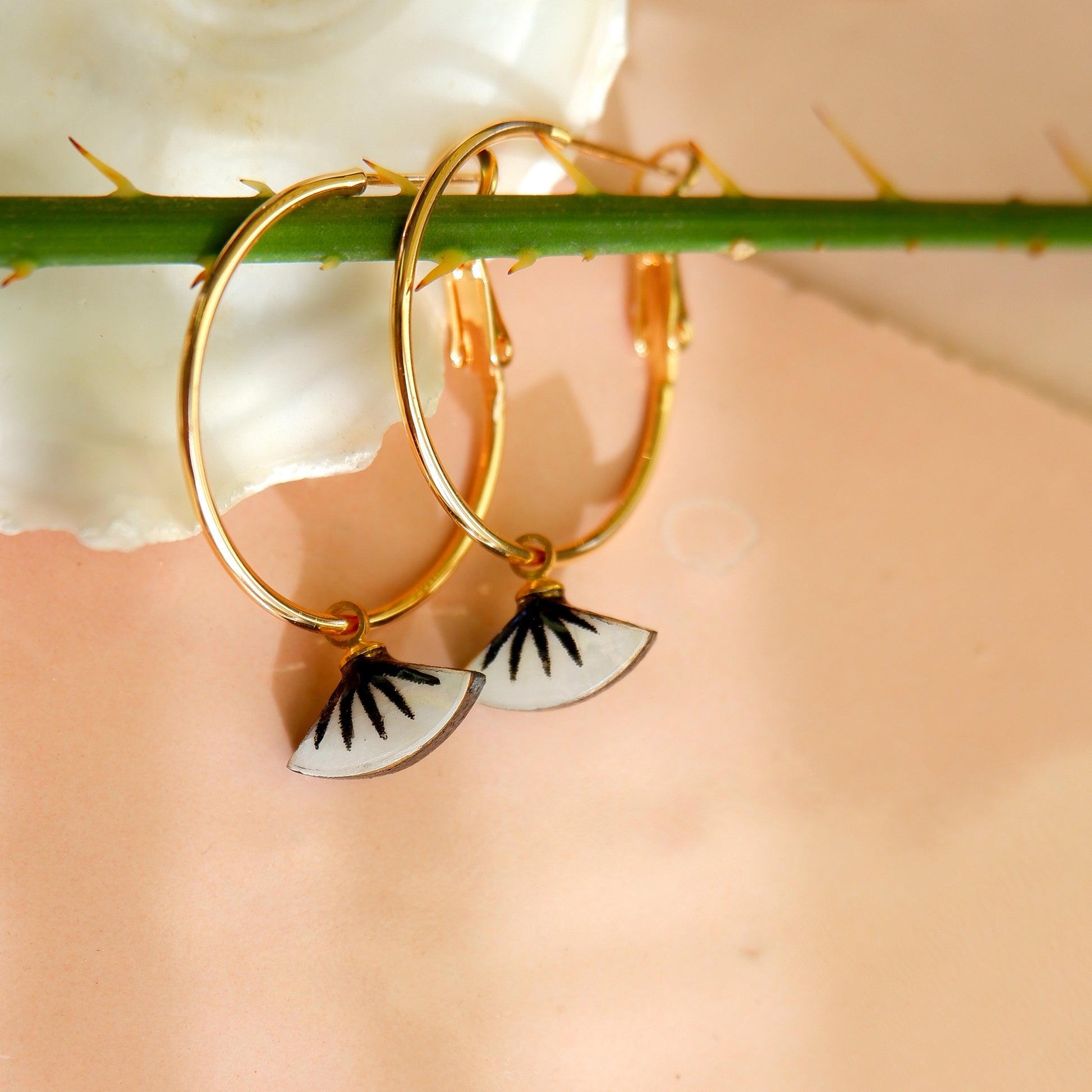 small gold hoop earrings with black spiky palm design on mother of pearl, in oyster shell