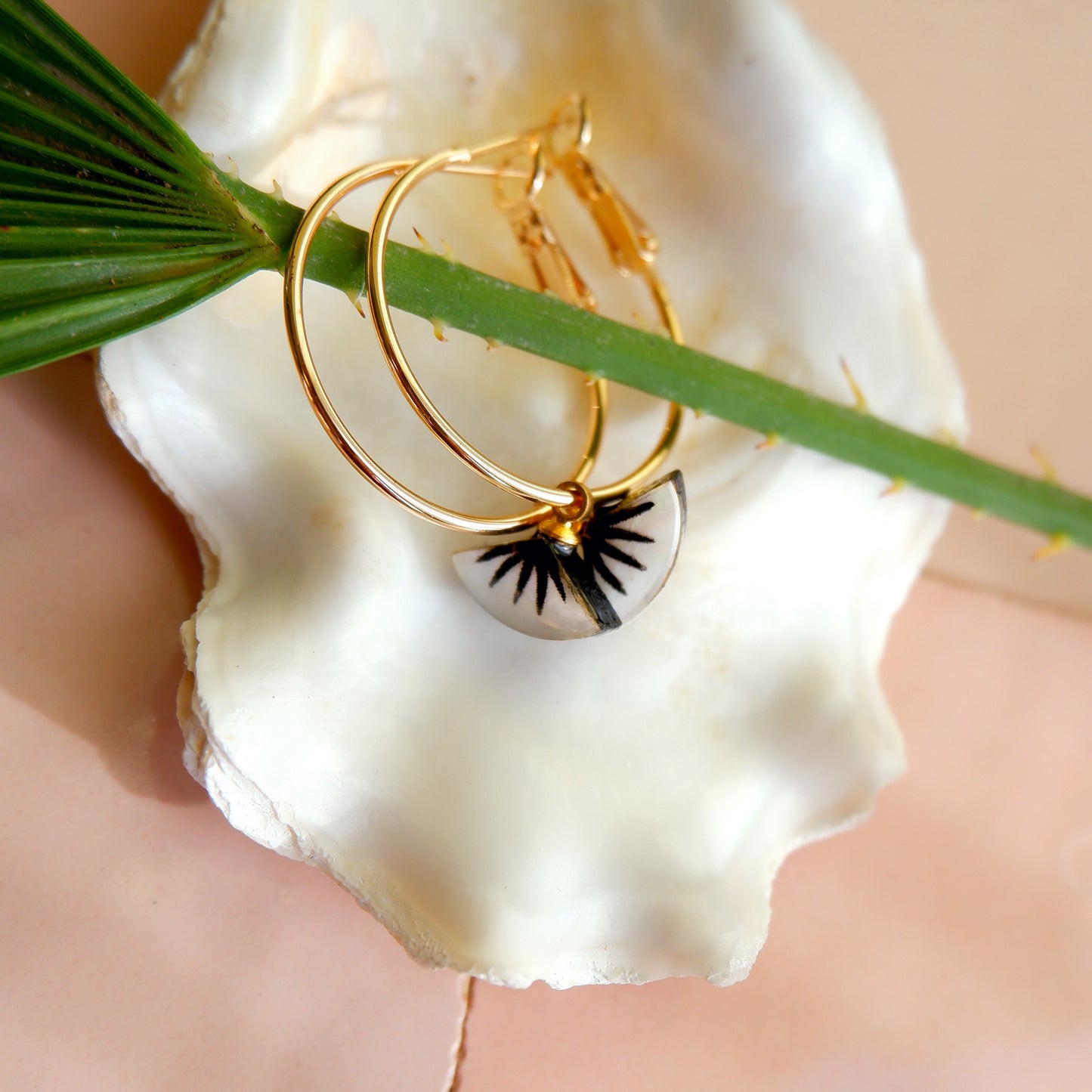 small gold hoop earrings with black spiky palm design on mother of pearl, in oyster shell
