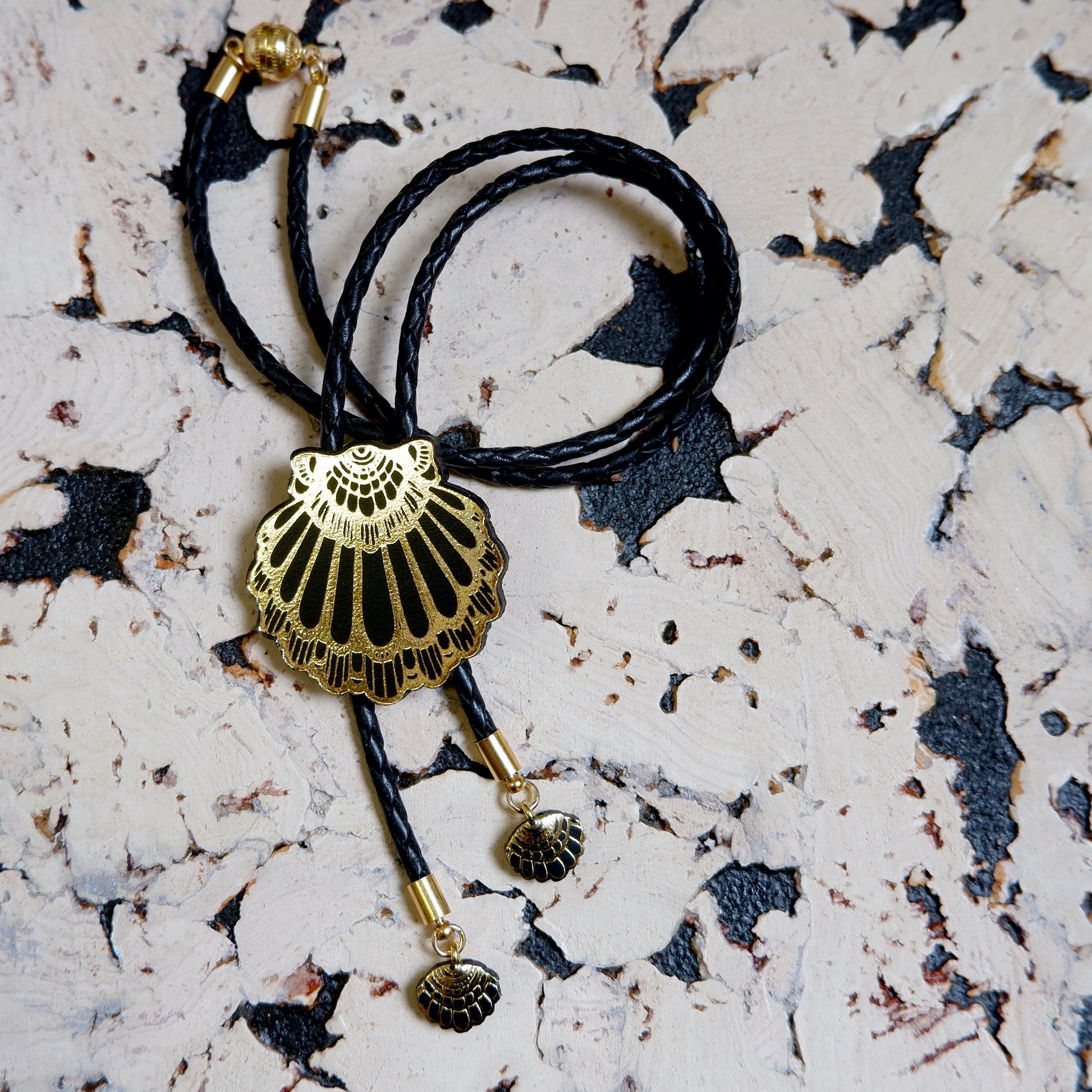 leather shell bolo necklace in black, on white & black cork background
