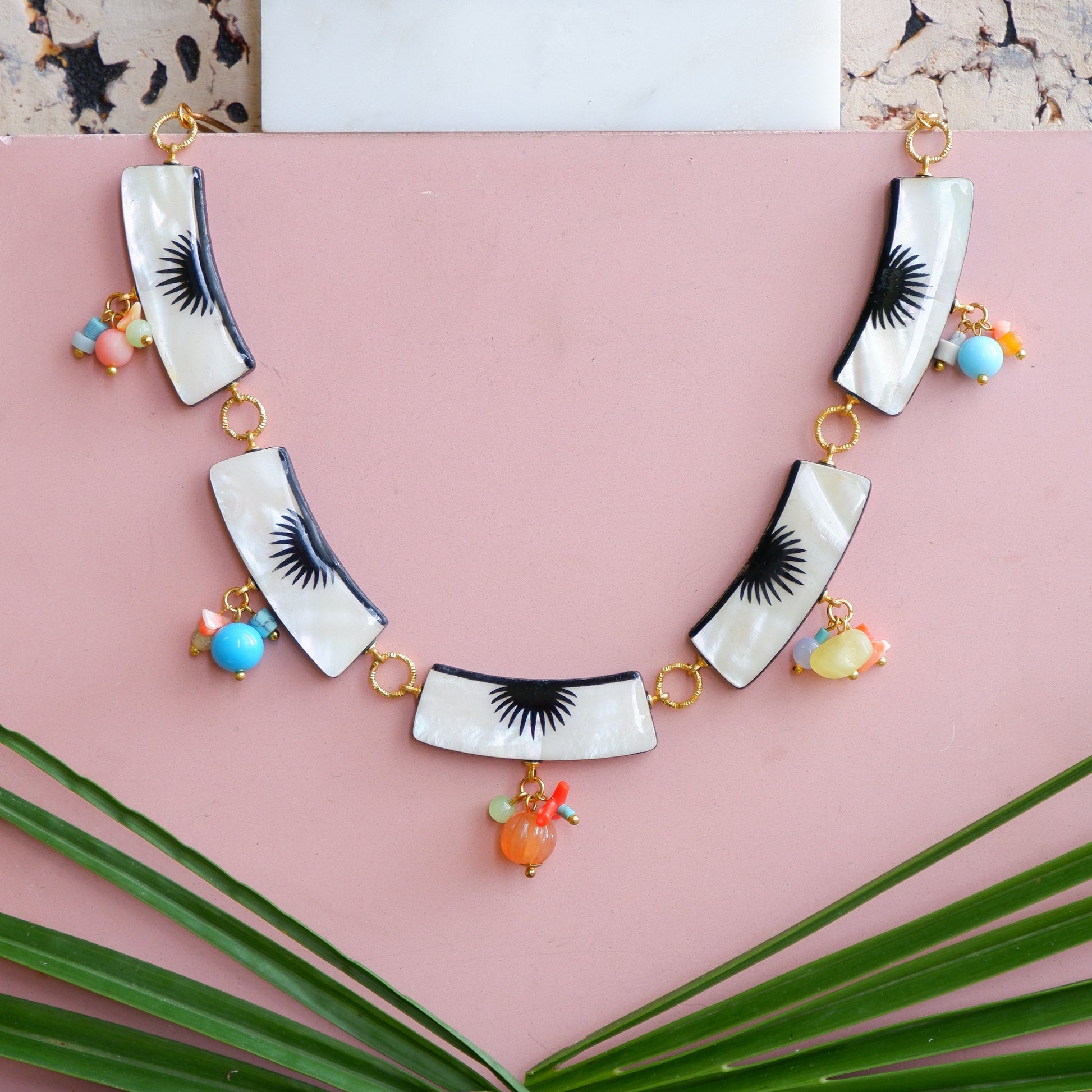 graphic black & white palm design mother of pearl collar necklace, with multi-coloured beads, pink background