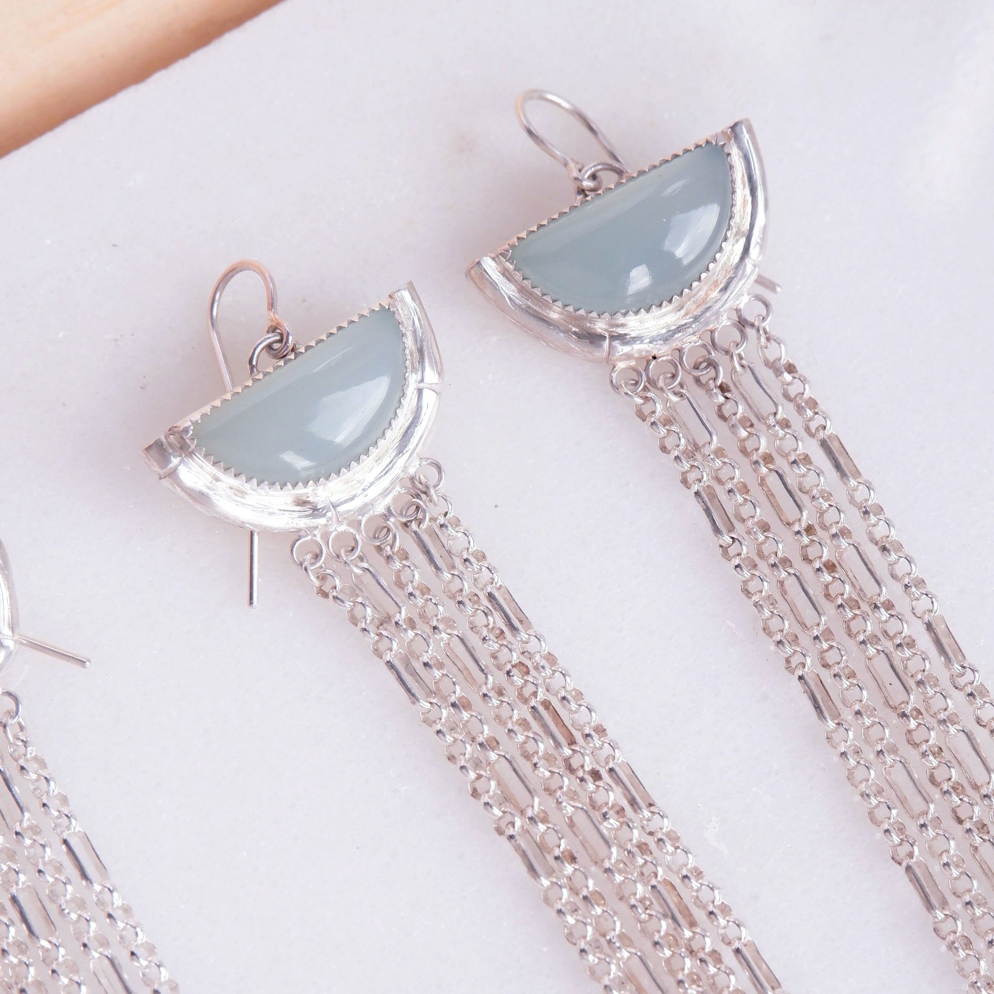 dramatic long chain fringe chandelier tassel earrings with half moon shaped semi precious aqua blue chalcedony gemstones,  cupped by solid silver bamboo hammock, with simple silver wire hooks. Close up cropped shot.