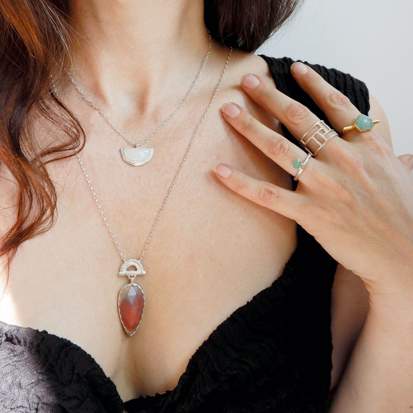 Pendant with long Pear-shaped faceted marbled red Botswana agate Gemstone hanging from silver Bamboo Arch, on fine silver chain. On model with half moon shaped moonstone pendant on silver chain, and selection of bamboo style rings in sterling silver & gold vermeil, with light green chrysoprase & turquoise Amazonite