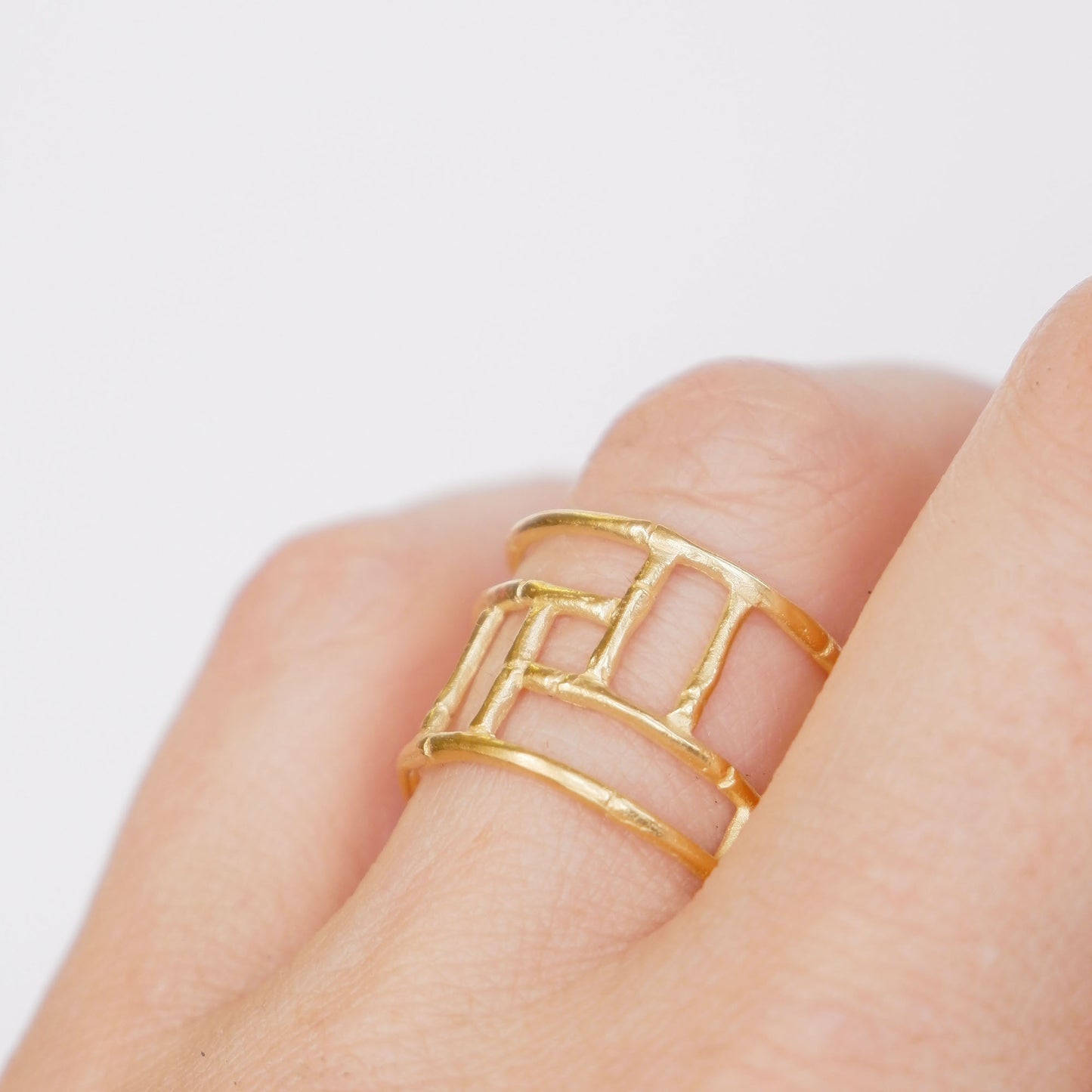 Wide Gold ring with geometric open-work Bamboo screen design, on a white background, on a hand