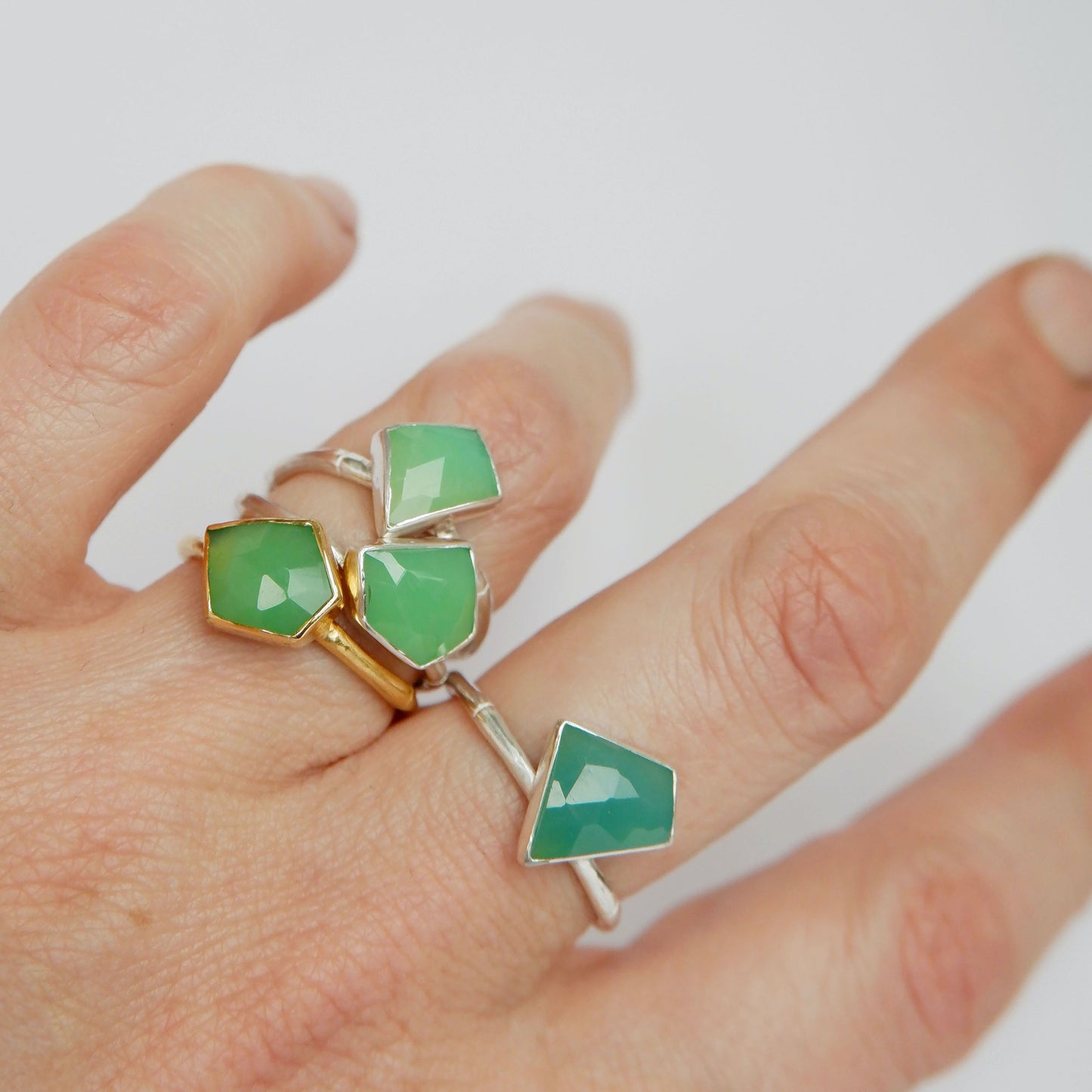 a stack of Sterling Silver and gold vermeil bamboo style rings with irregular angular geometric Chrysoprase gem stones in different shades of green, on a hand, against a white background