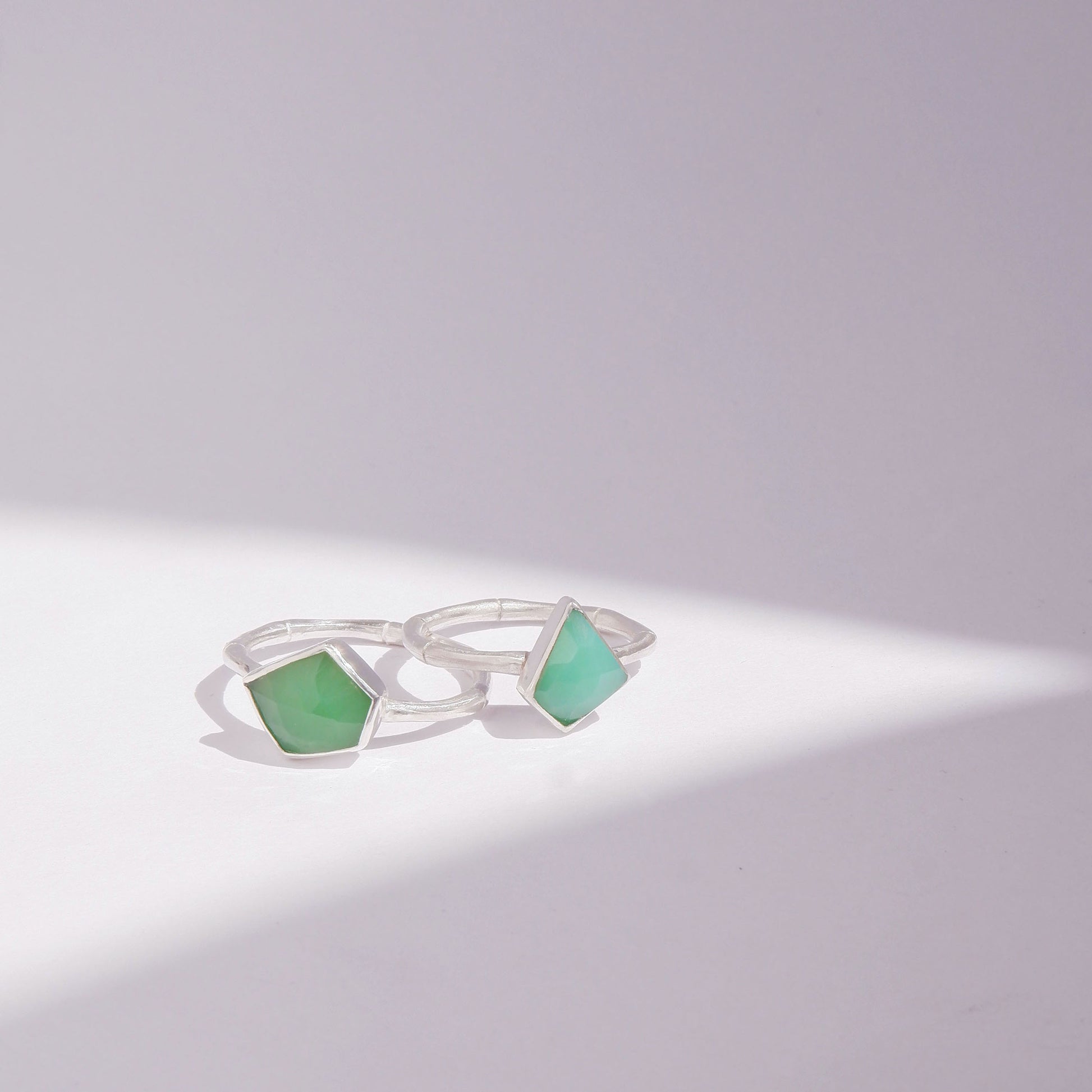 a pair of Sterling Silver bamboo style rings with irregular angular geometric Chrysoprase gem stones in different shades of green, against a white background