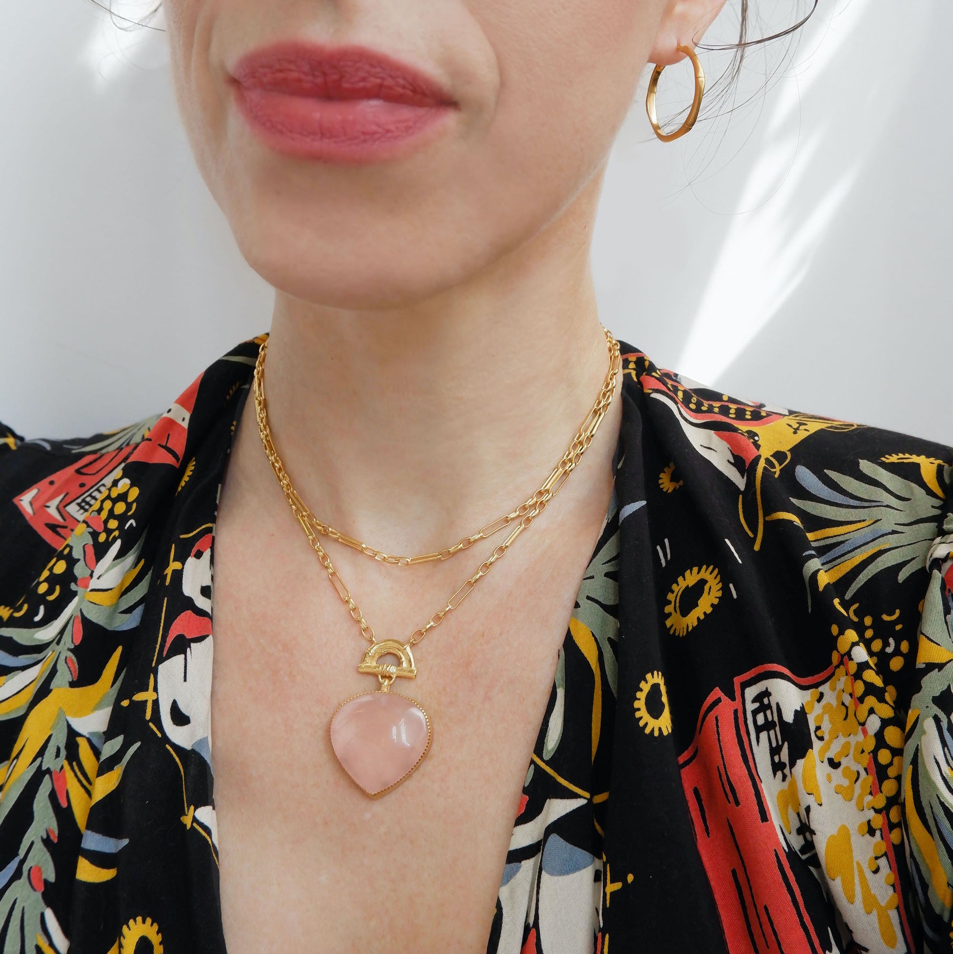 Gold double chain necklace with a rose pink quartz heart-shaped pendant with golden bamboo arch detail, on a person, against a white background