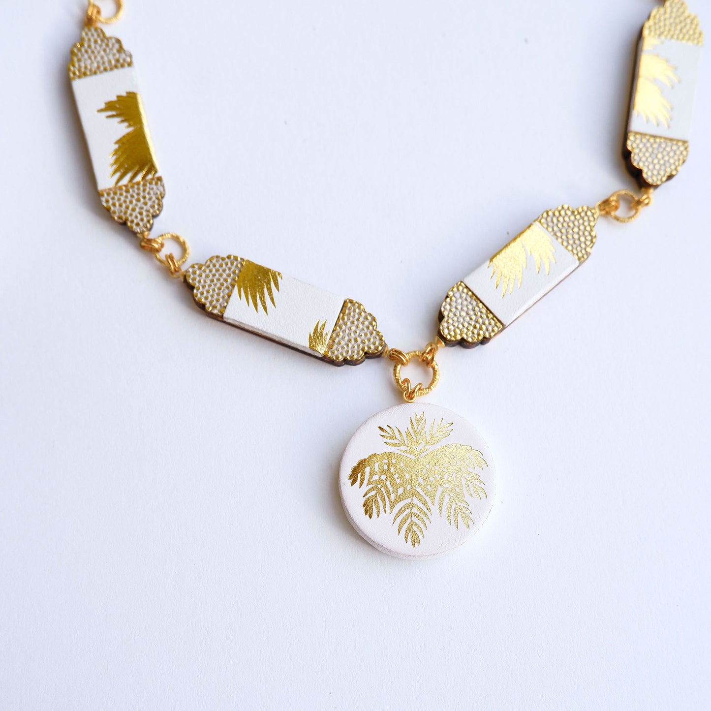 white leather necklace, with six sections & medallion pendant.. Gold Palm print on white leather, with embossed dot pattern detail., close up