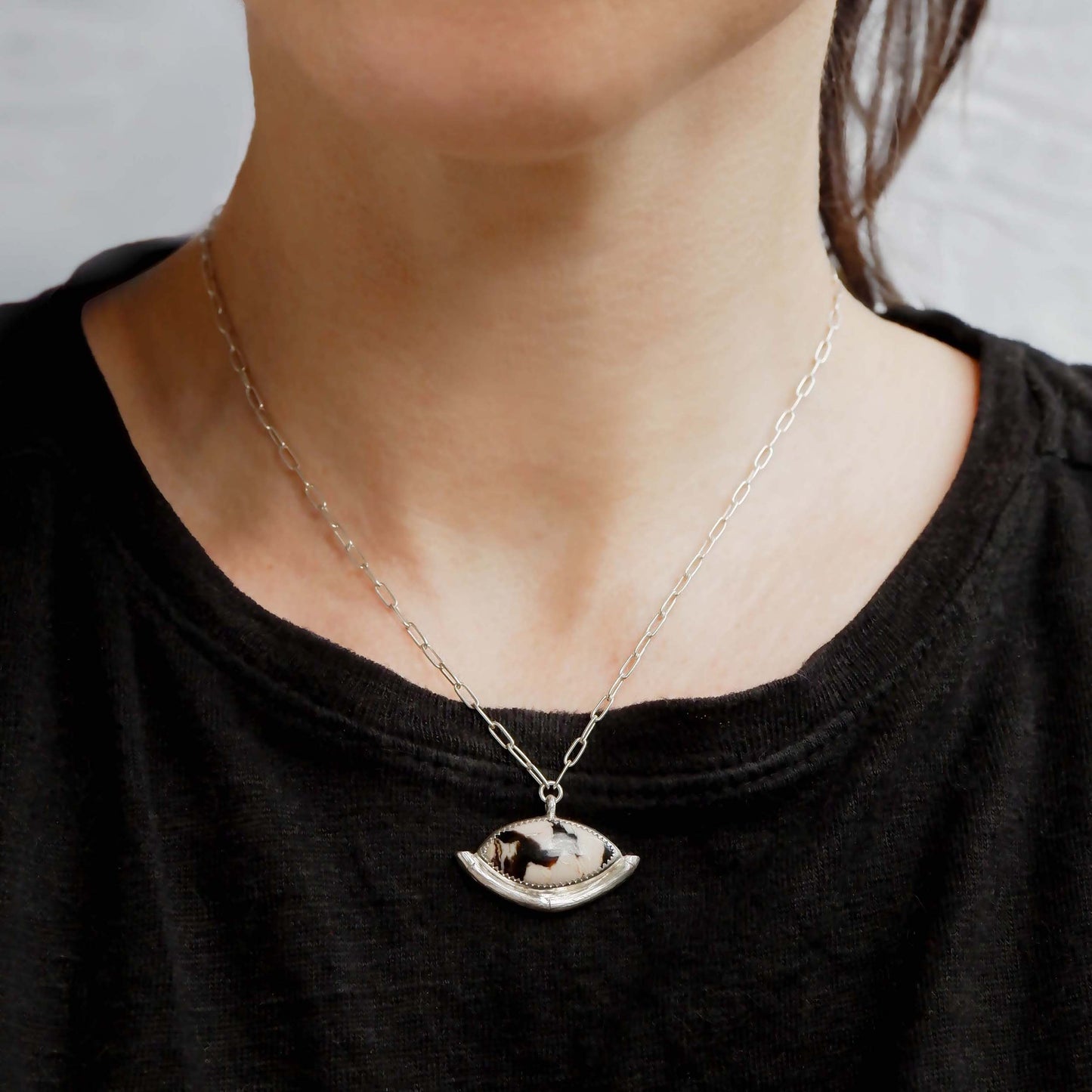 Sterling Silver gemstone Pendant on short paperclip style chain. The pendant features a marquise-cut peanut Wood Cabochon with a striking zigzag pattern in black & white, a serrated sterling silver bezel, and a bamboo style halo mount, cupping the stone. Shown on model, for scale, in black t shirt.