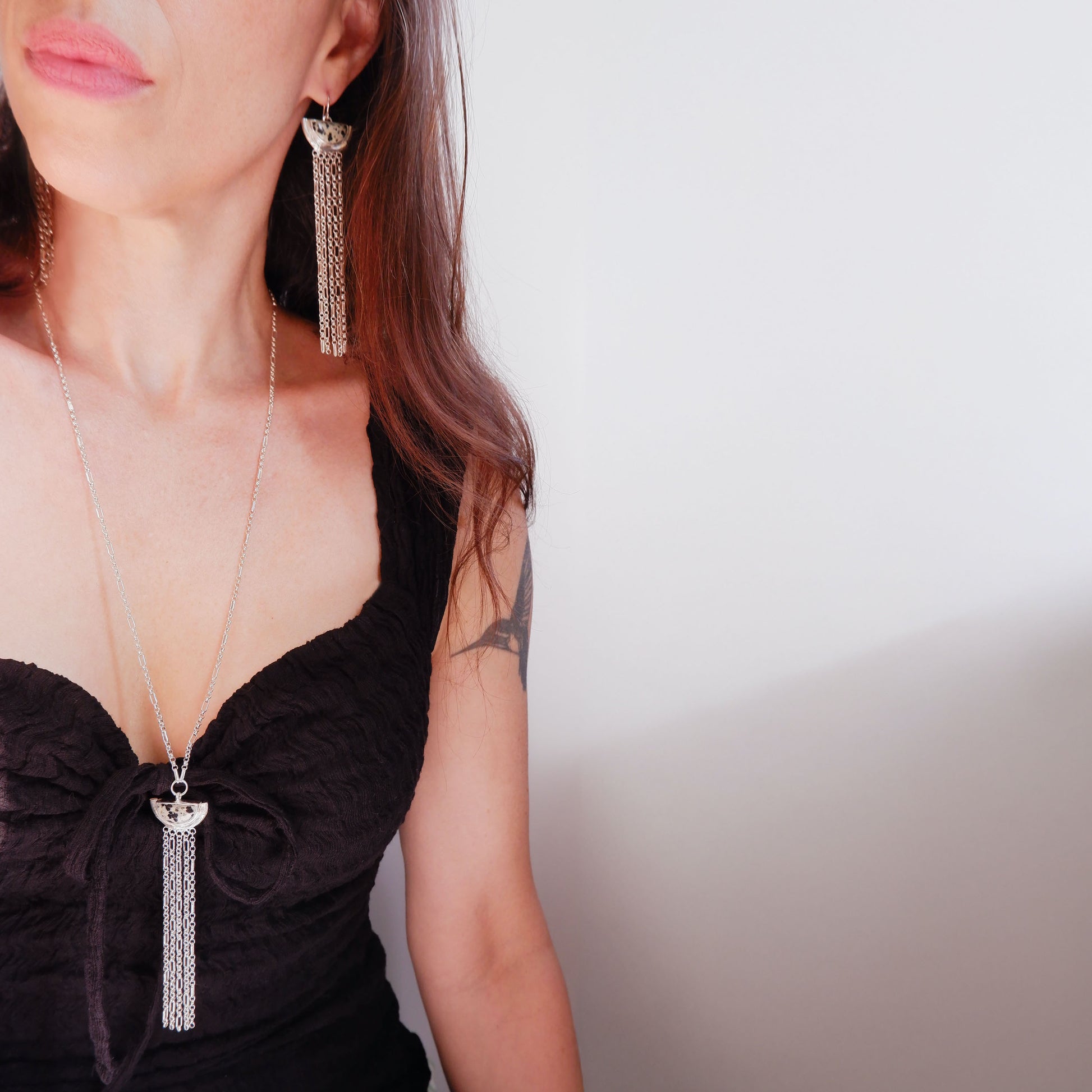 dramatic long chain fringe chandelier tassel earrings with half moon shaped semi precious speckled Dalmatian Jasper gemstones,  cupped by solid silver bamboo hammock, with simple sterling silver wire hooks. Shown on model wearing matching long Dalmatian Jasper silver chain tassel pendant necklace.