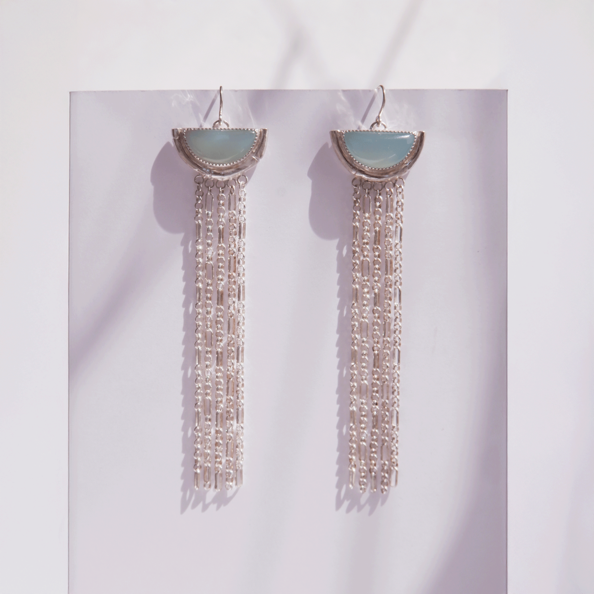 dramatic long chain fringe chandelier tassel earrings with half moon shaped semi precious Aqua Blue Chalcedony gemstones,  cupped by solid silver bamboo hammock, with simple silver wire hooks. An animated gif showing the earrings in bright sunlight & diffused light.