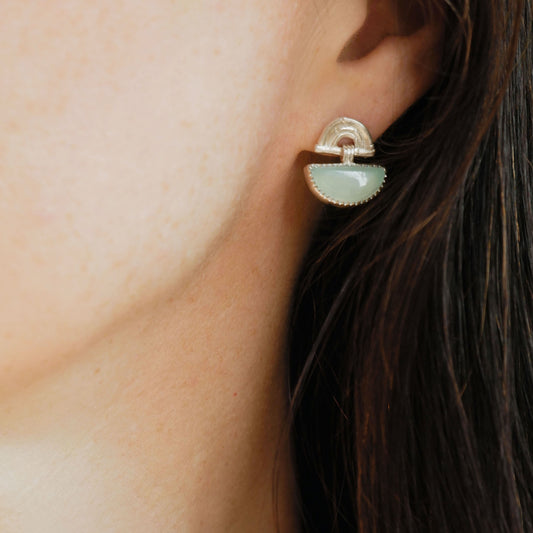 small stud earrings in sterling silver, featuring triple arches of bamboo, hung with a half moon shaped Chalcedony gemstone, set with silver teeth, on model