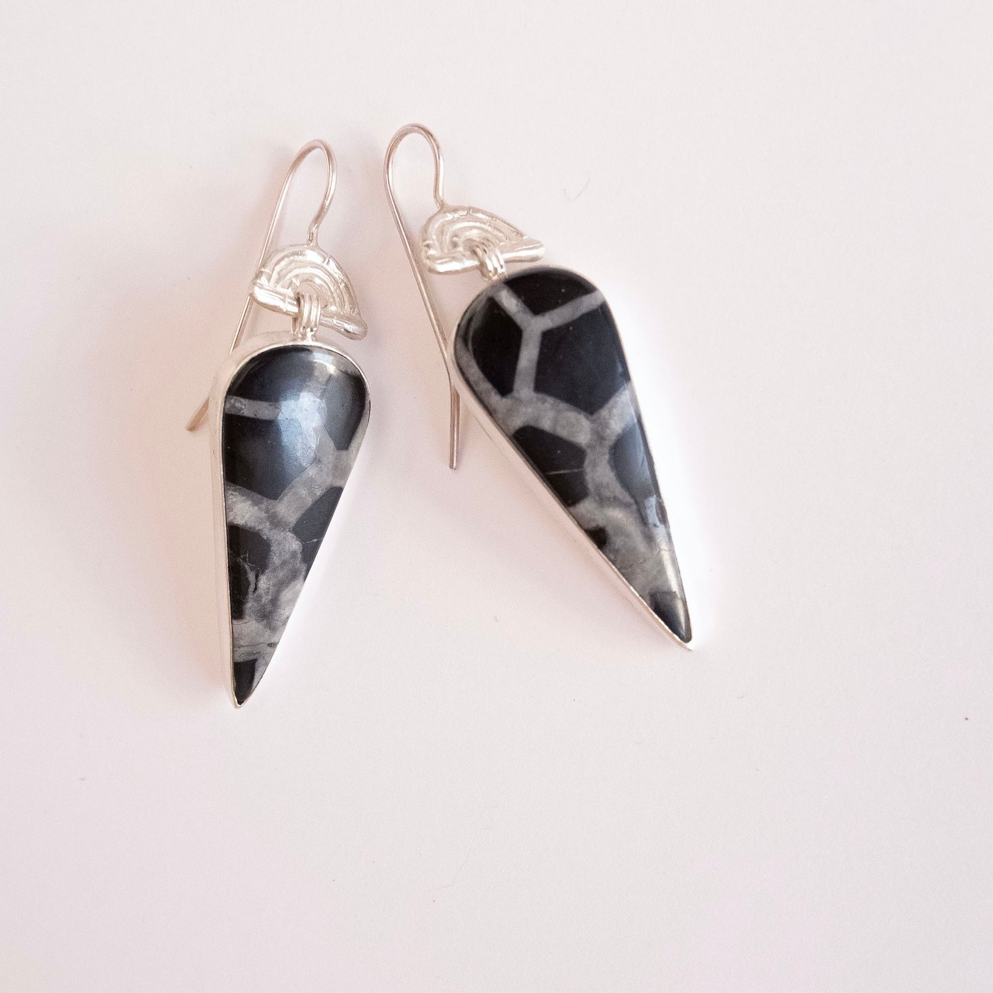 drop earrings in sterling silver, featuring triple arches of bamboo on hook fittings, hung with long pear/teardrop shaped black septarian gemstone pendants.