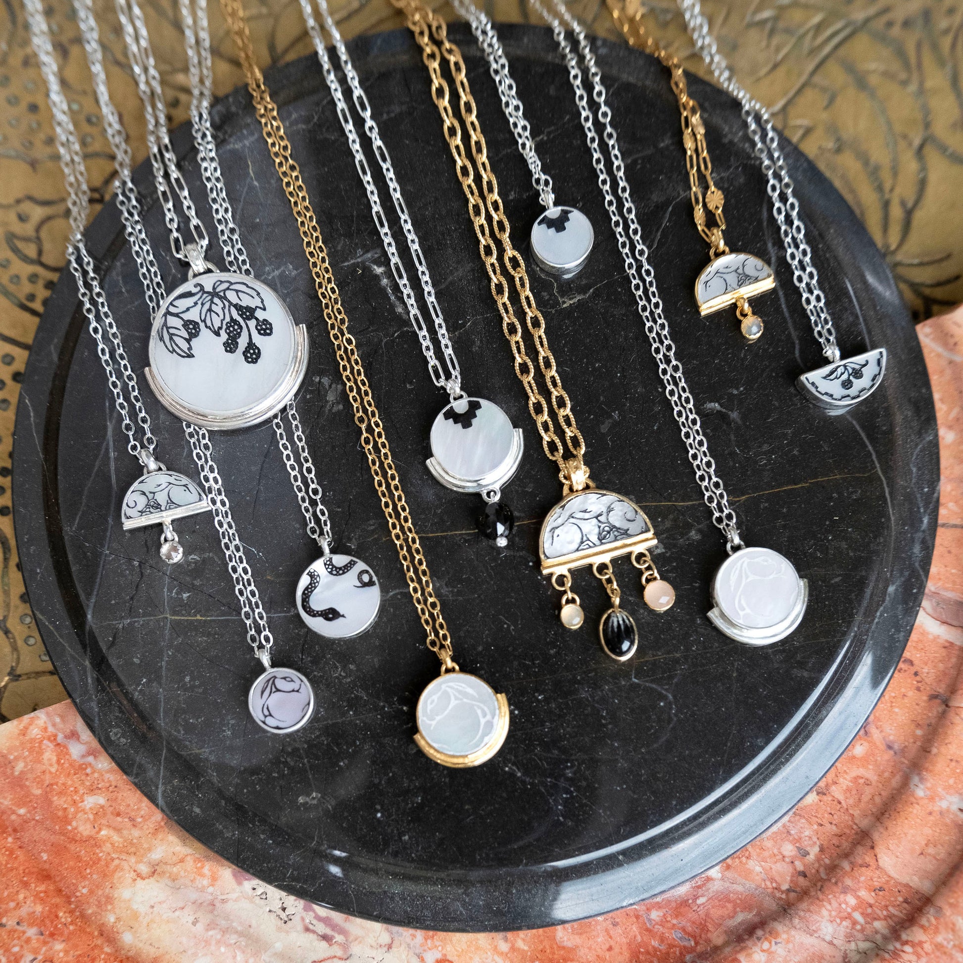 a display of full moon & half moon shaped mother of pearl pendants, in different sizes & styles, all with engraved patterns on the surface, in sterling silver & gold vermeil. Photographed on black marble.