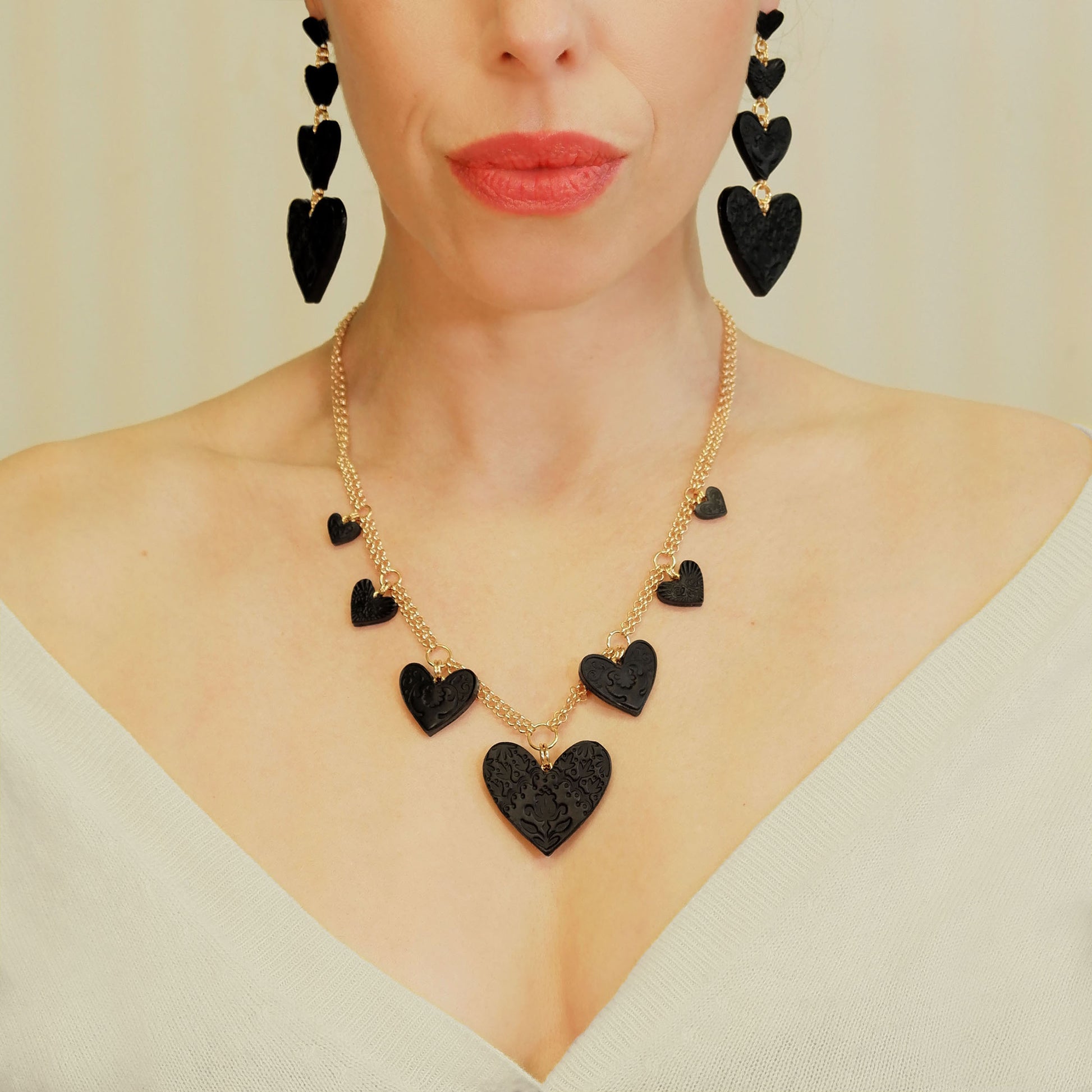 Large charm necklace, featuring 4 sizes of smooth Black Leather Hearts; each embossed with a different folk-art inspired floral design, on double gold-plated belcher chain. On model, with matching earrings