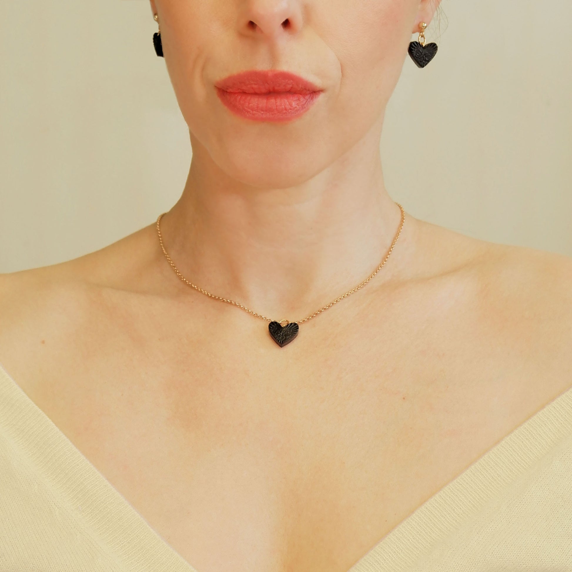 small Black Leather Heart pendant; embossed with a  rose & rays design, on fine gold-plated belcher chain, on model, with matching black heart earrings