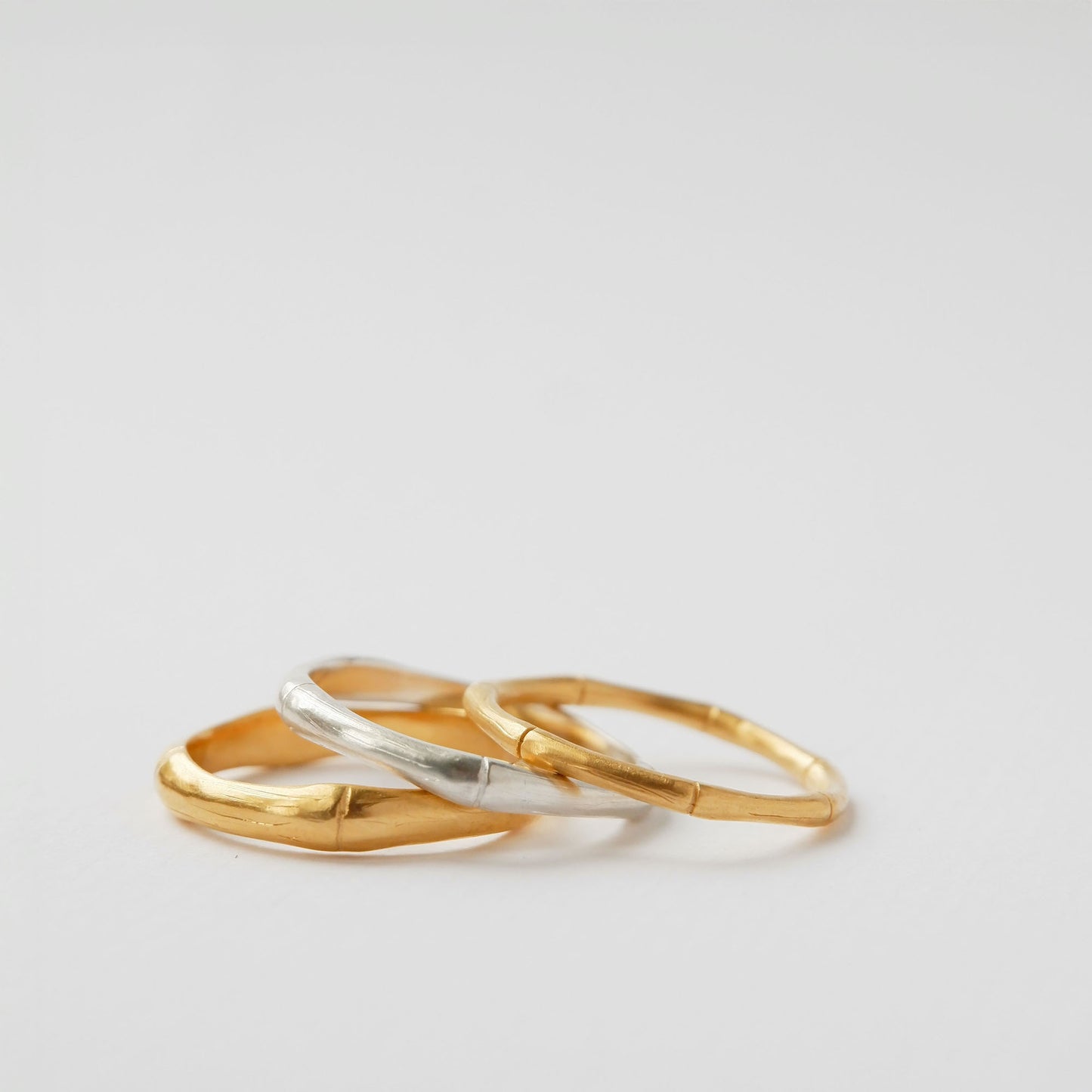 A pile of three bamboo style stacking rings, in three thicknesses in Sterling Silver & Gold Vermeil, white background