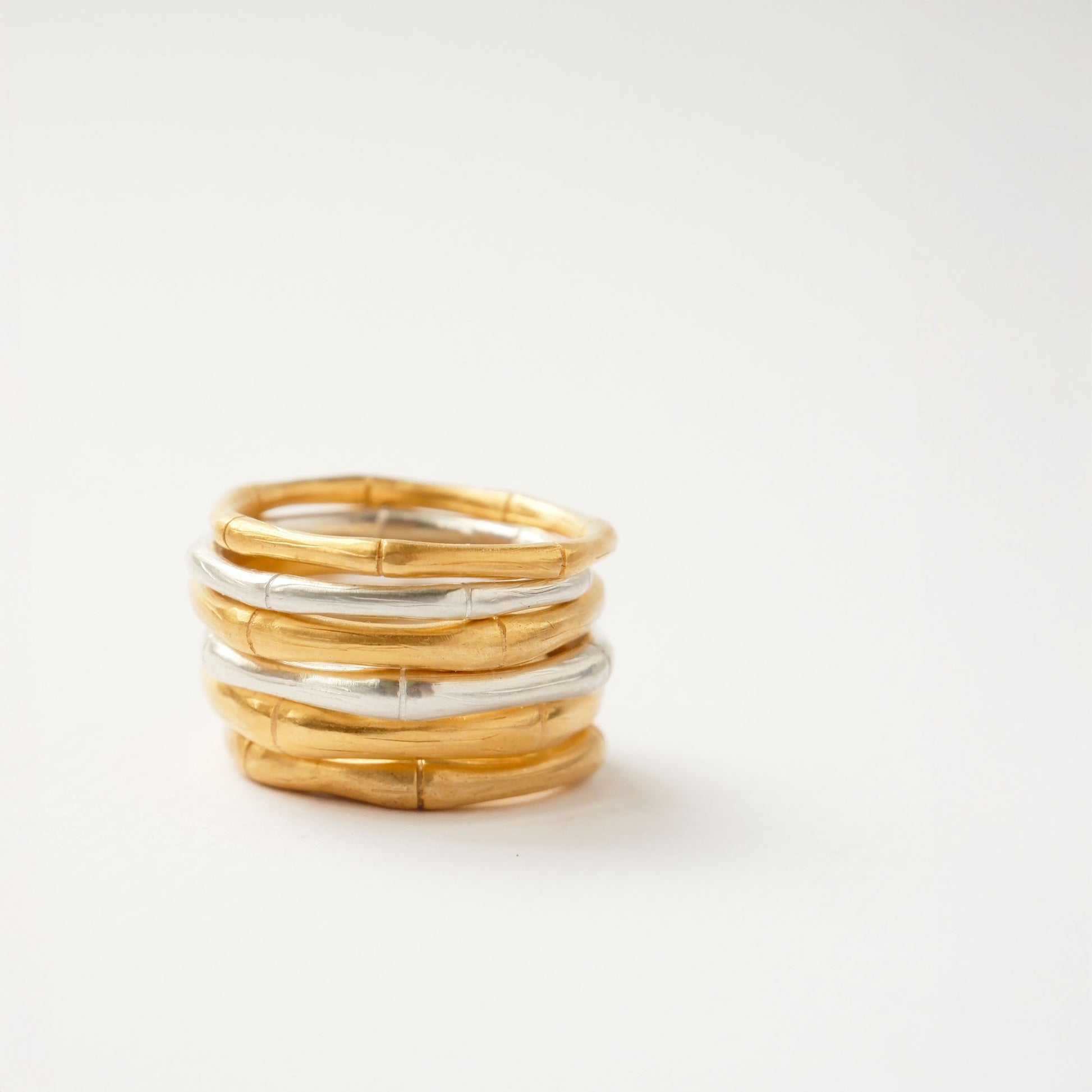 A pile of  bamboo style stacking rings, in three thicknesses in Sterling Silver & Gold Vermeil, white background