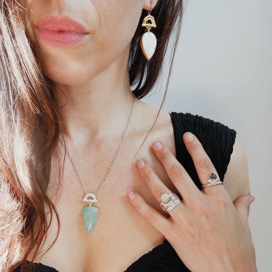 structural open-work ring in a bamboo style, featuring a faceted round  golden brown Montana Agate gemstone in a scalloped setting. Sterling Silver. shown on model for scale, with another sterling silver bamboo style ring with pointed gemstone, arched bamboo earring & pendant necklace with pear shaped gemstone drops charms.