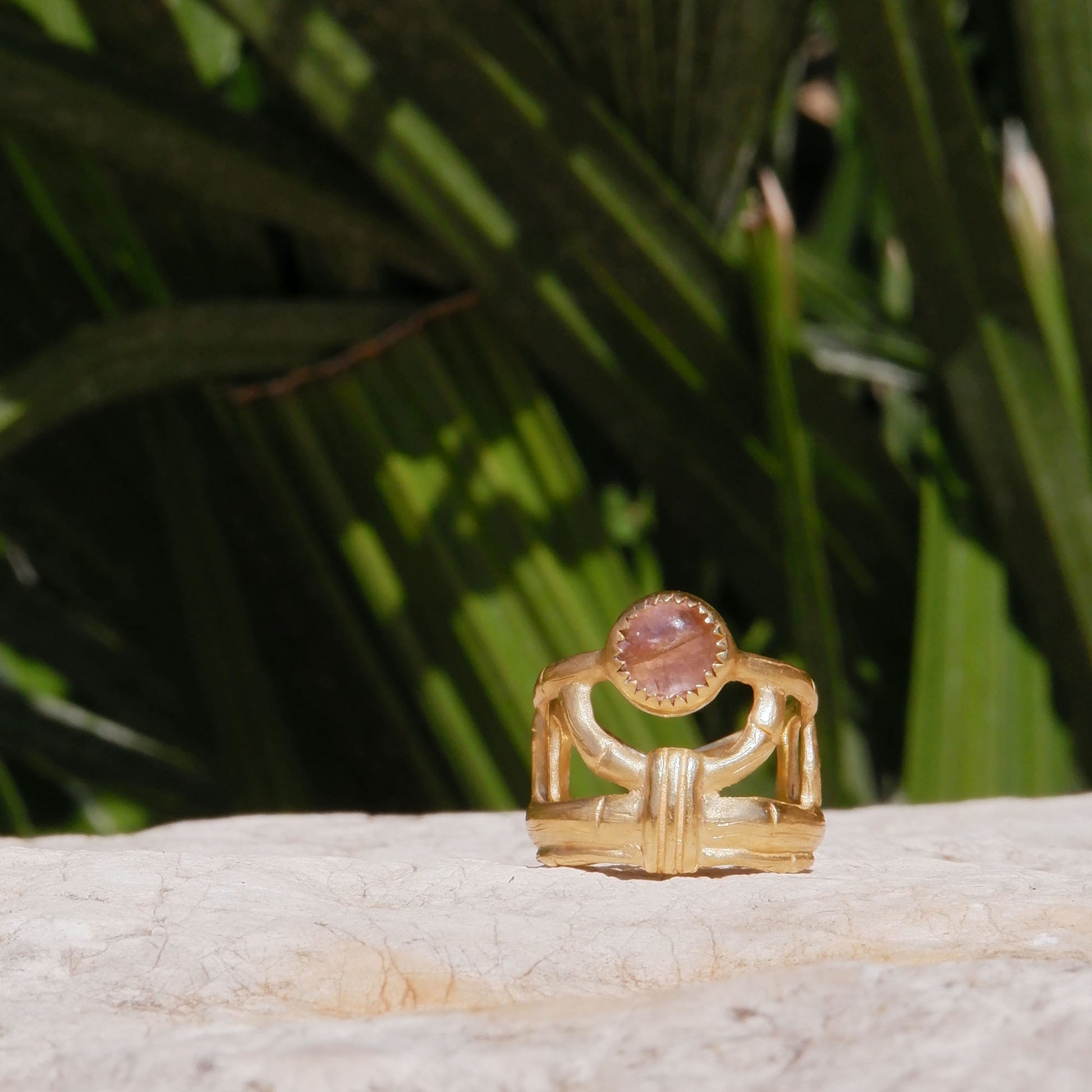 structural open-work ring in a bamboo style, featuring round pale peachy pink Tourmaline cabochon gemstone in a serrated setting. Gold Vermeil. Shown sitting on a rock