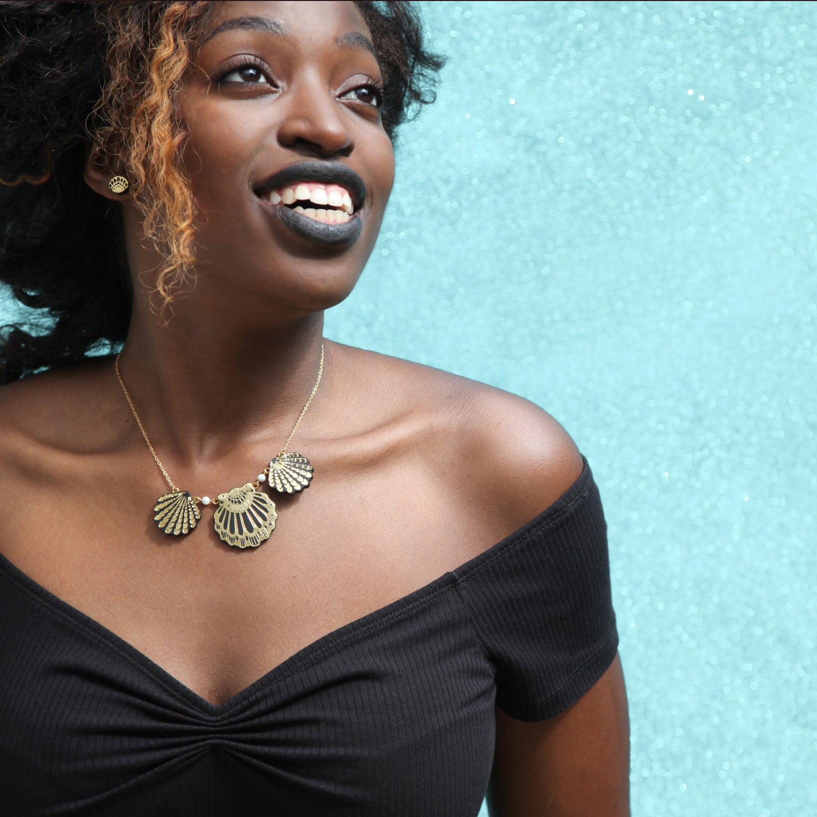 model wearing black & gold leather shell necklace & earrings, aqua glitter background