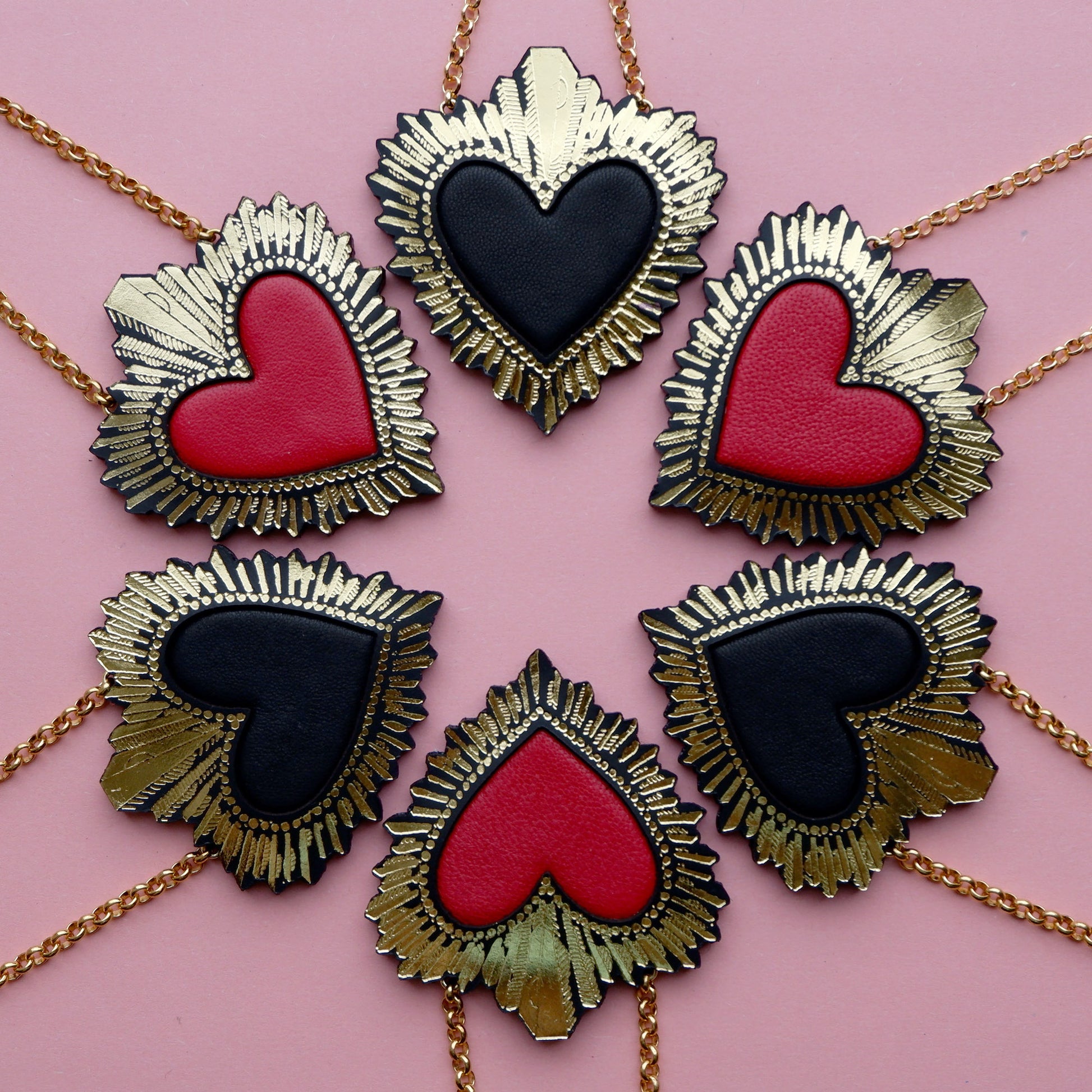 display of red and black leather sacred heart pendant necklaces, on gold belcher chain, on pink background