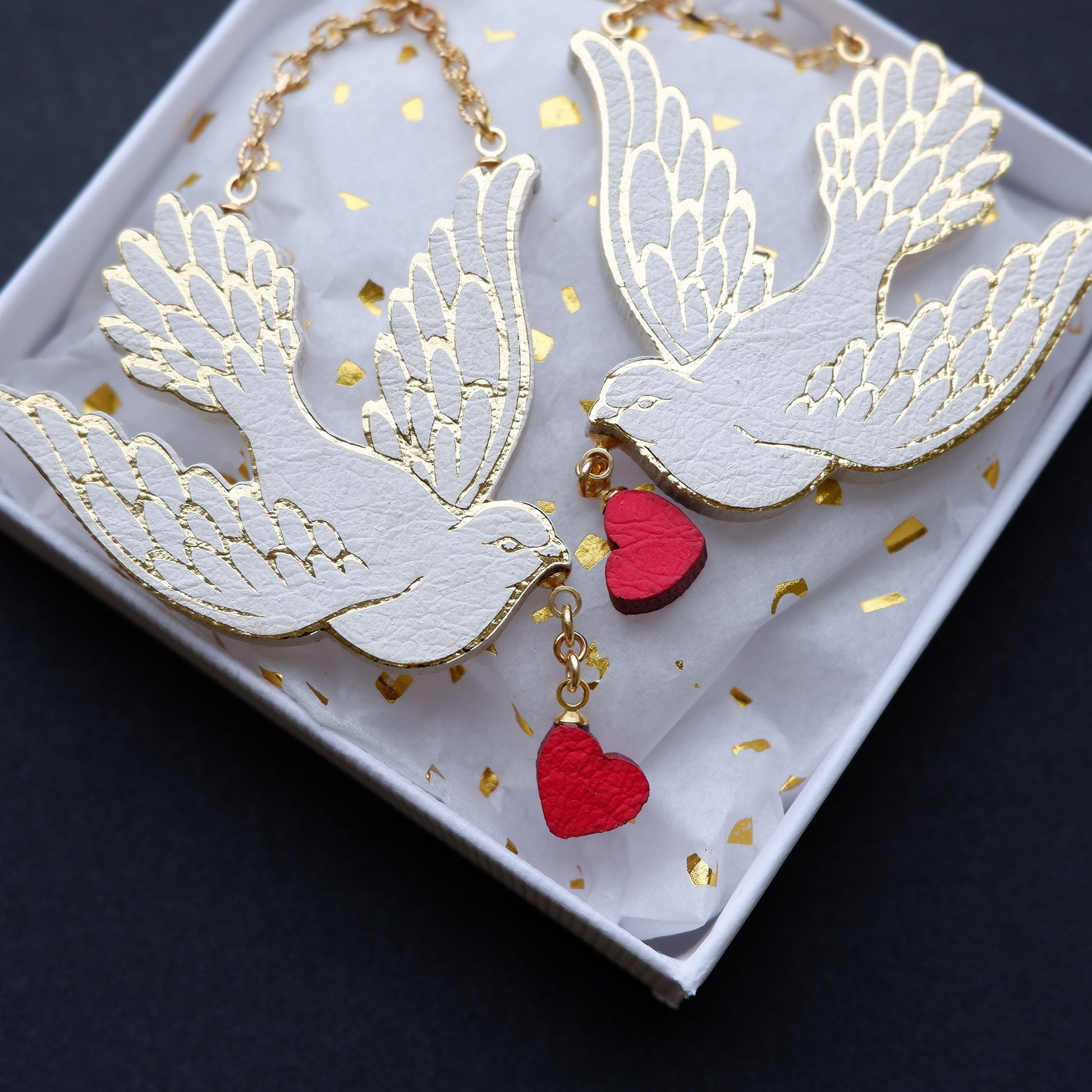 white dove earrings carrying small red hearts from their beaks.