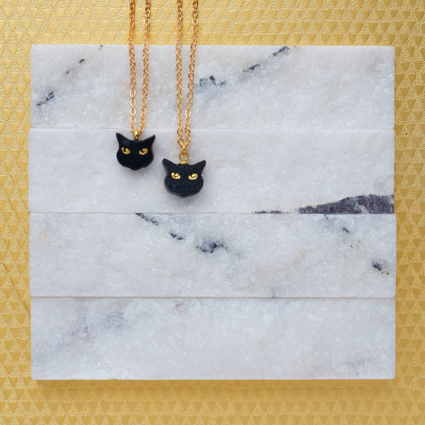 litle black cat head pendants on fine gold chain. 1 is leather, 1 is plant based