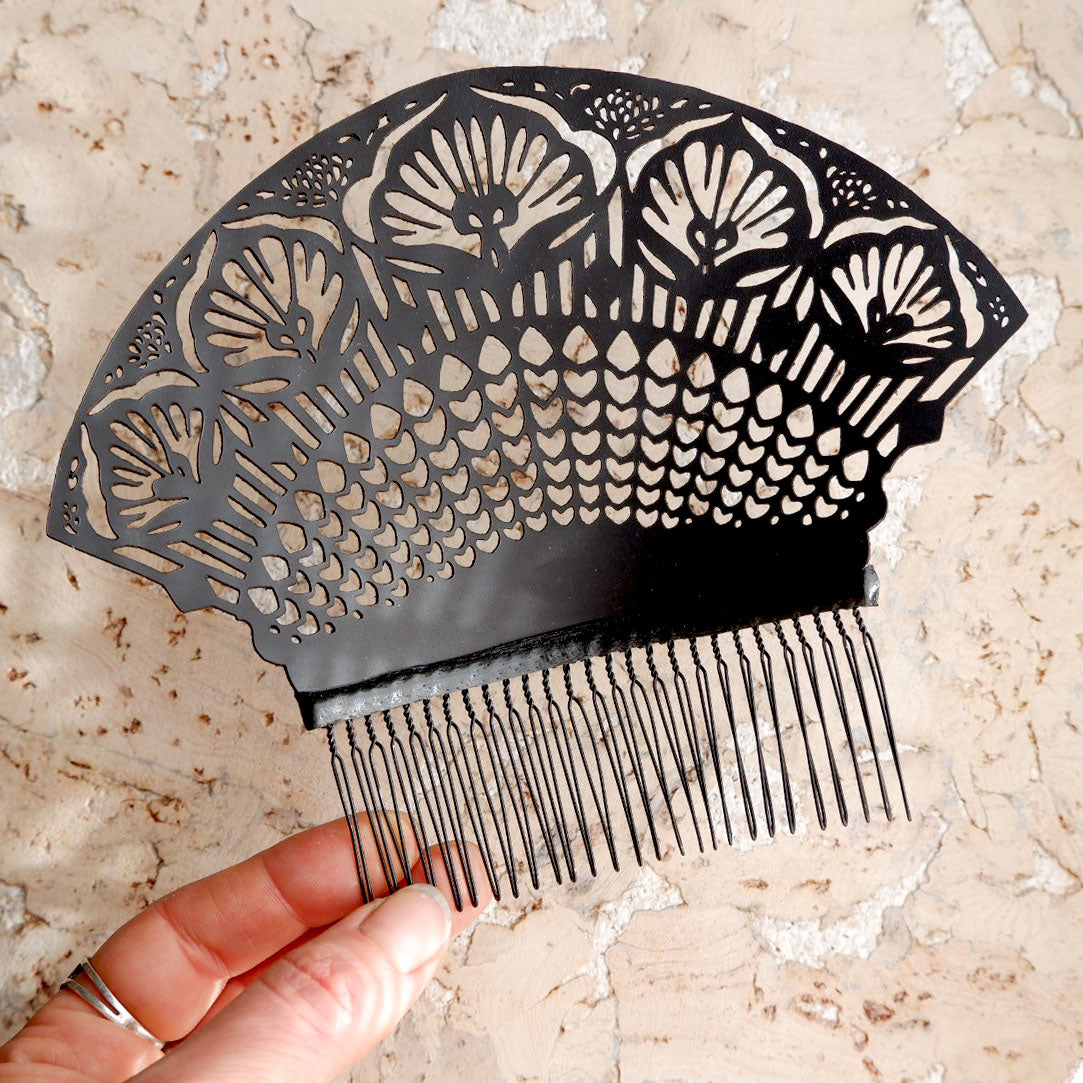 black laser-cut lace style leather hair combs, held in a hand